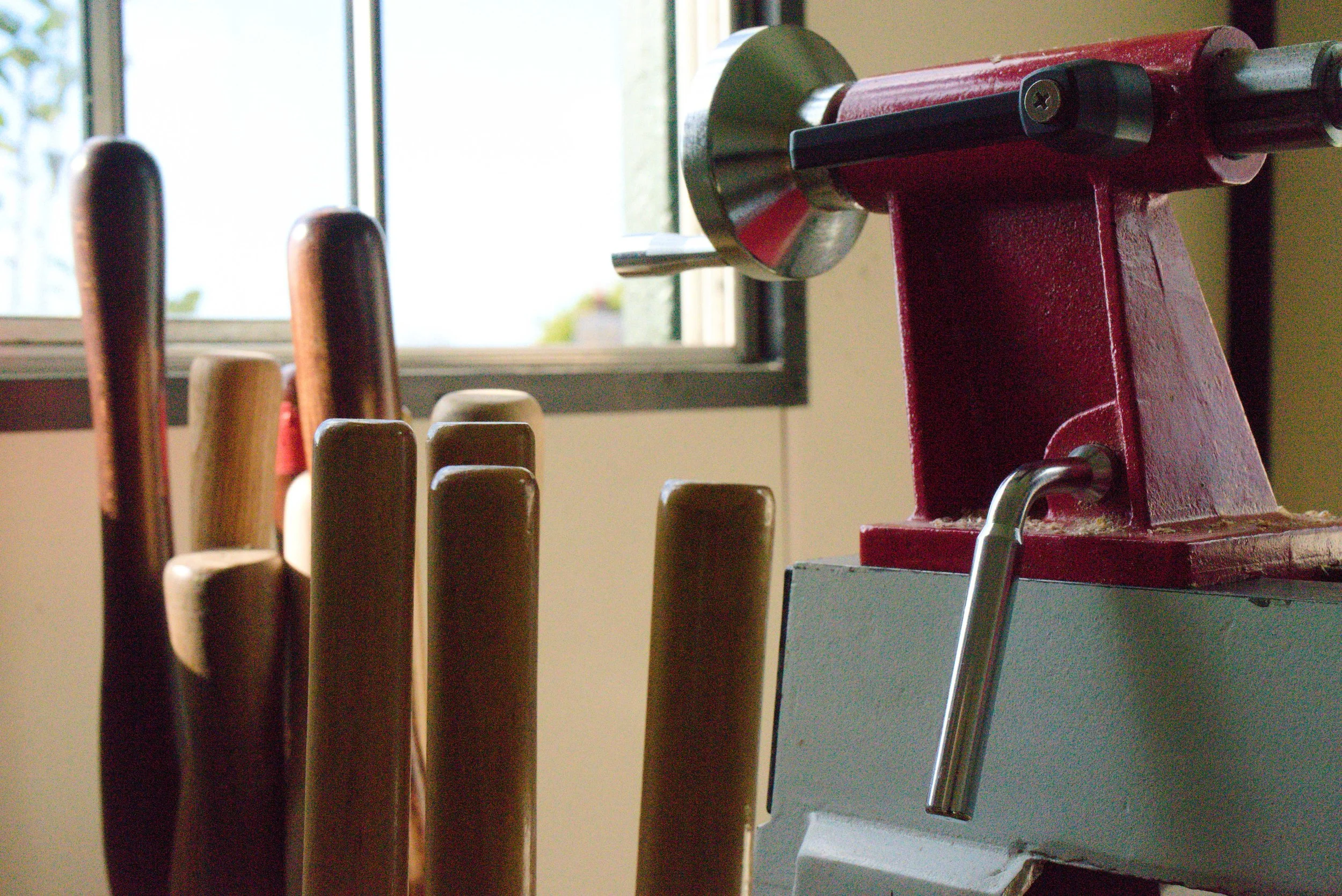 A red meat slicer and several stacked wooden chairs near a window in a room.