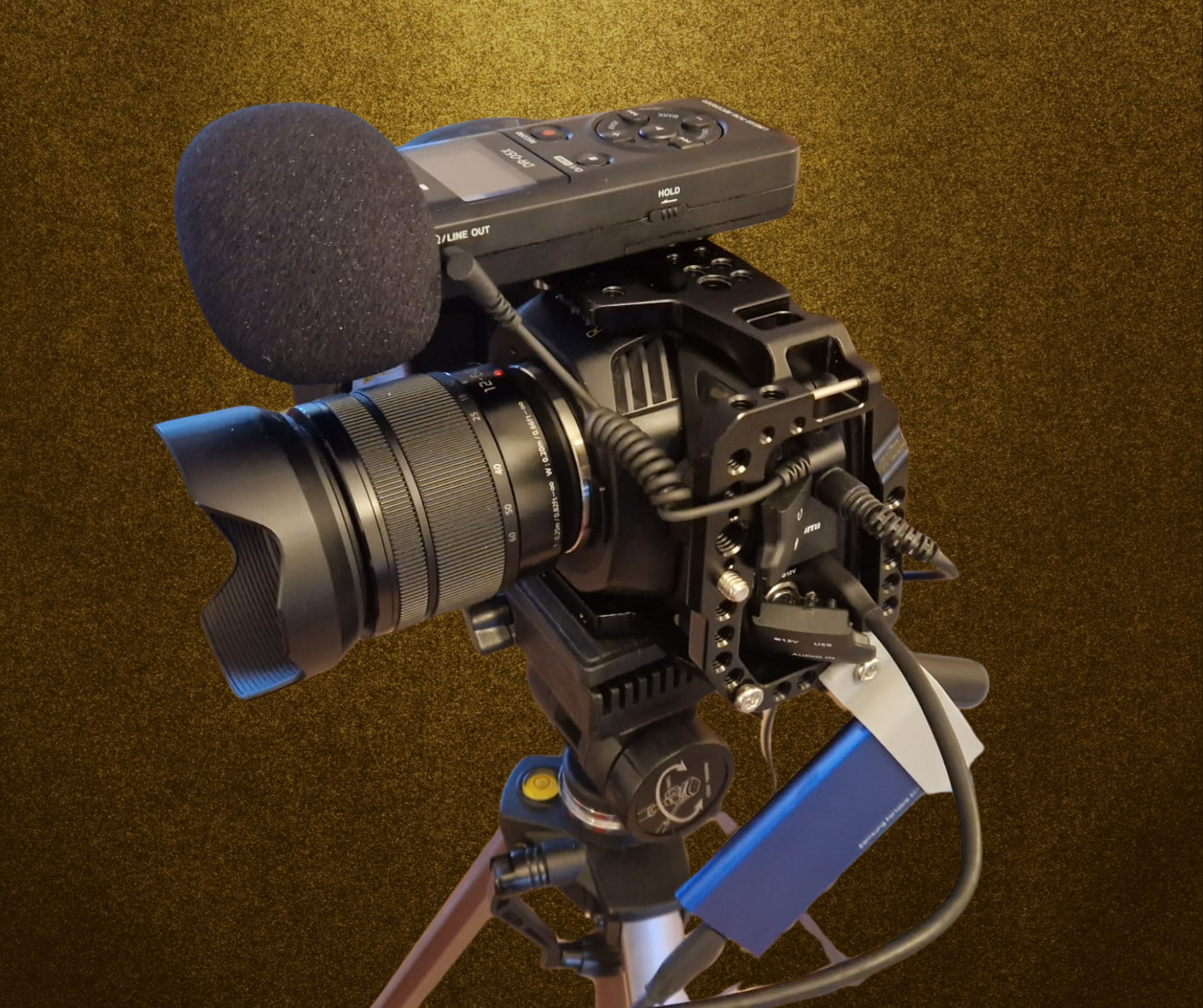 Video camera with a mounted microphone on a tripod against a brown background.