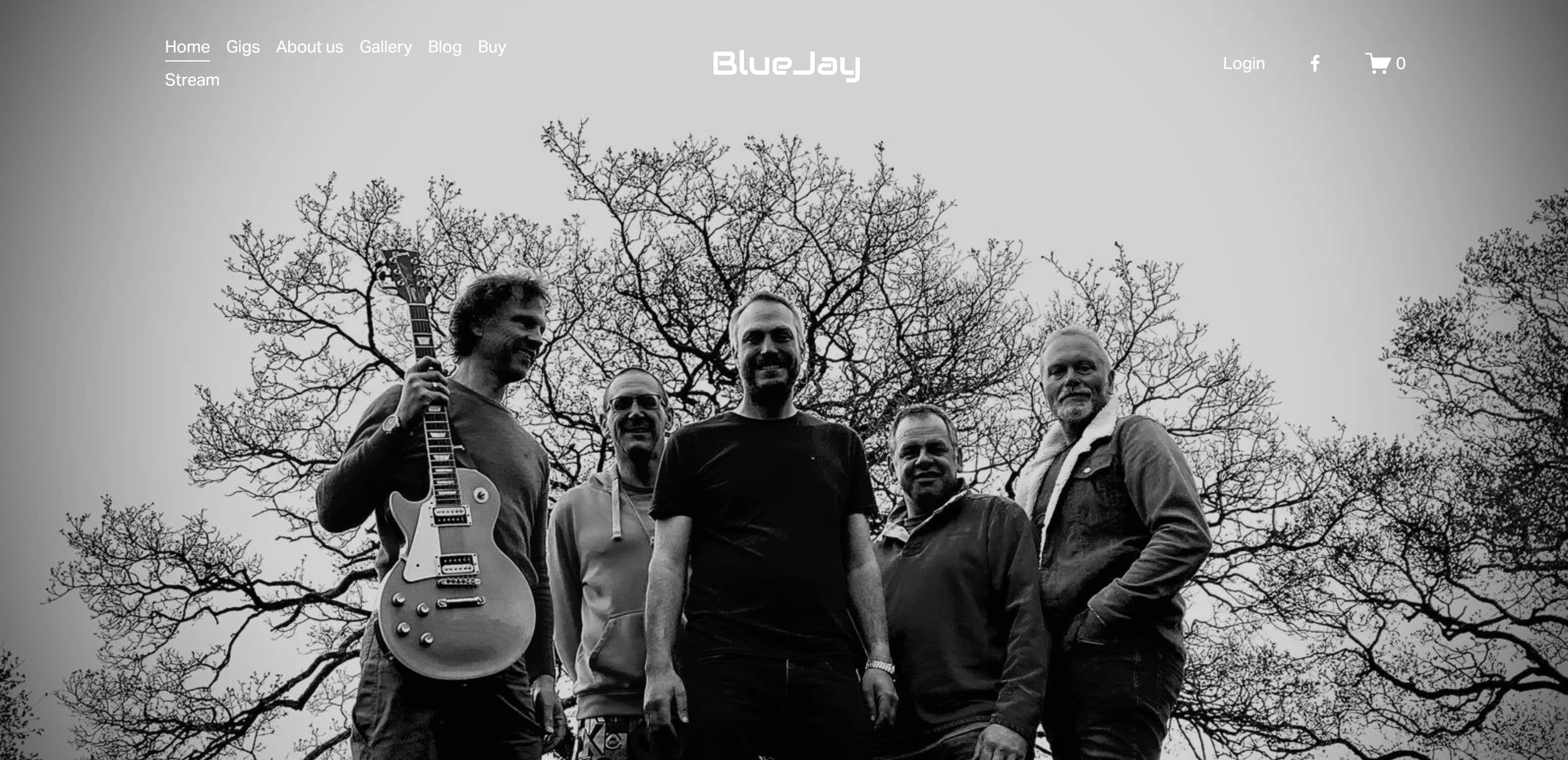 Black and white photo of five men standing outdoors in front of leafless trees, one holding an electric guitar, smiling at the camera.