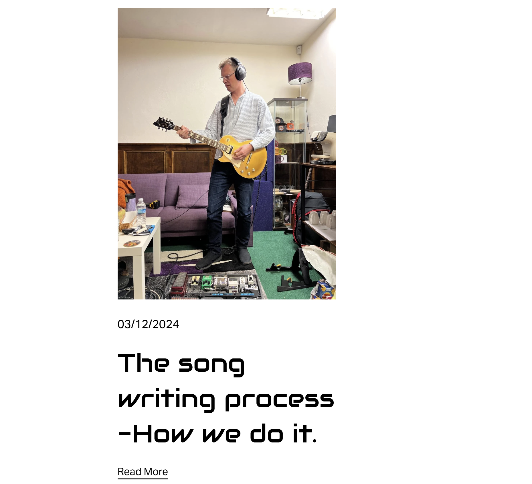 A man wearing headphones and glasses playing an electric guitar in a room with a purple sofa, a white coffee table, a shelf with various items, and a guitar pedalboard on the floor.