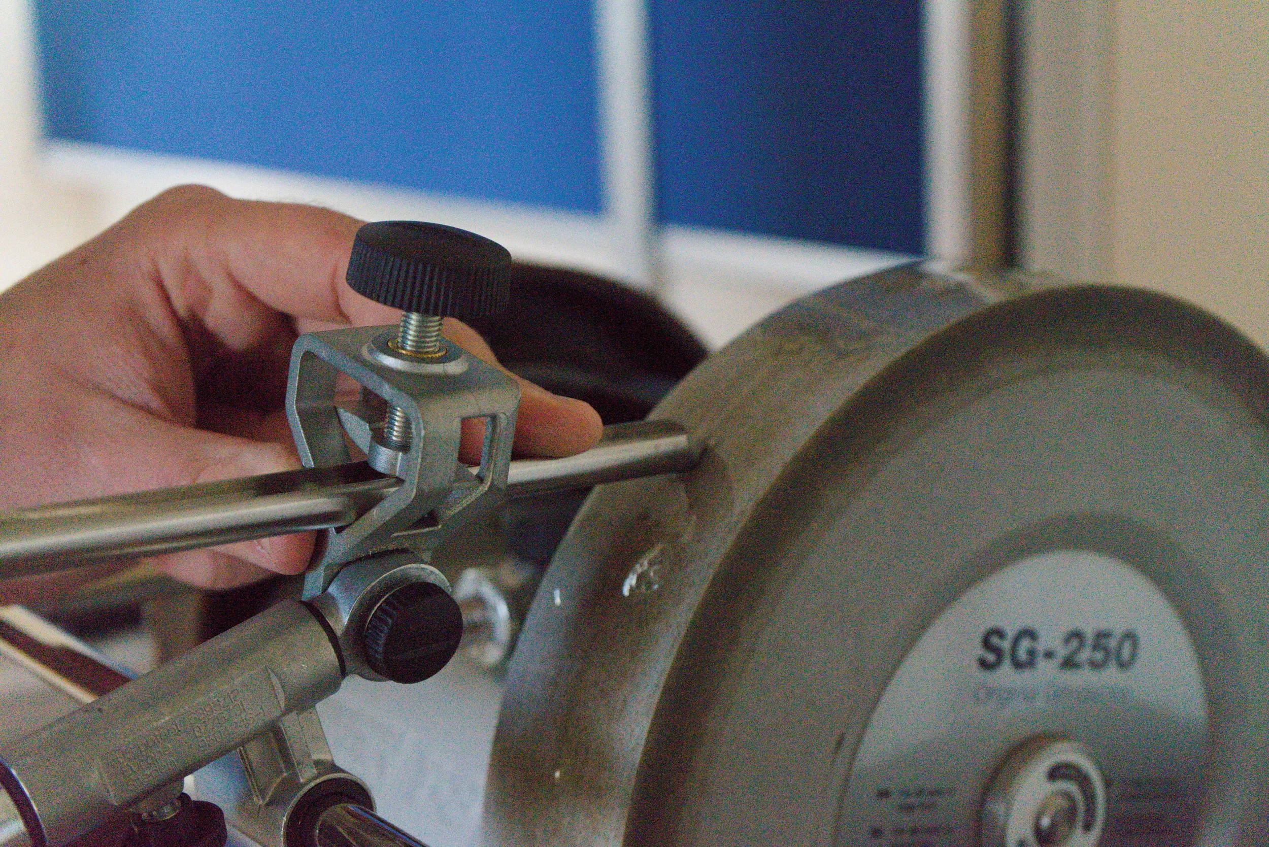 A person adjusting the clamp of a metal grinding machine labeled SG-250.