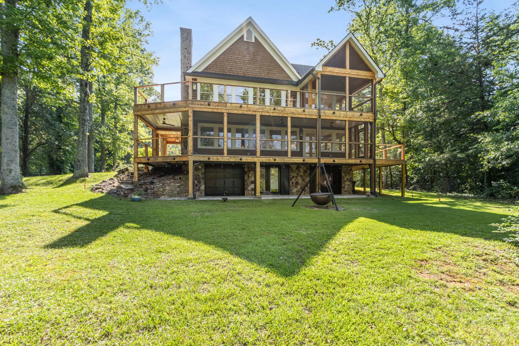 Covered porch with wooden flooring and large screened windows overlooking a green yard with trees and a lake.