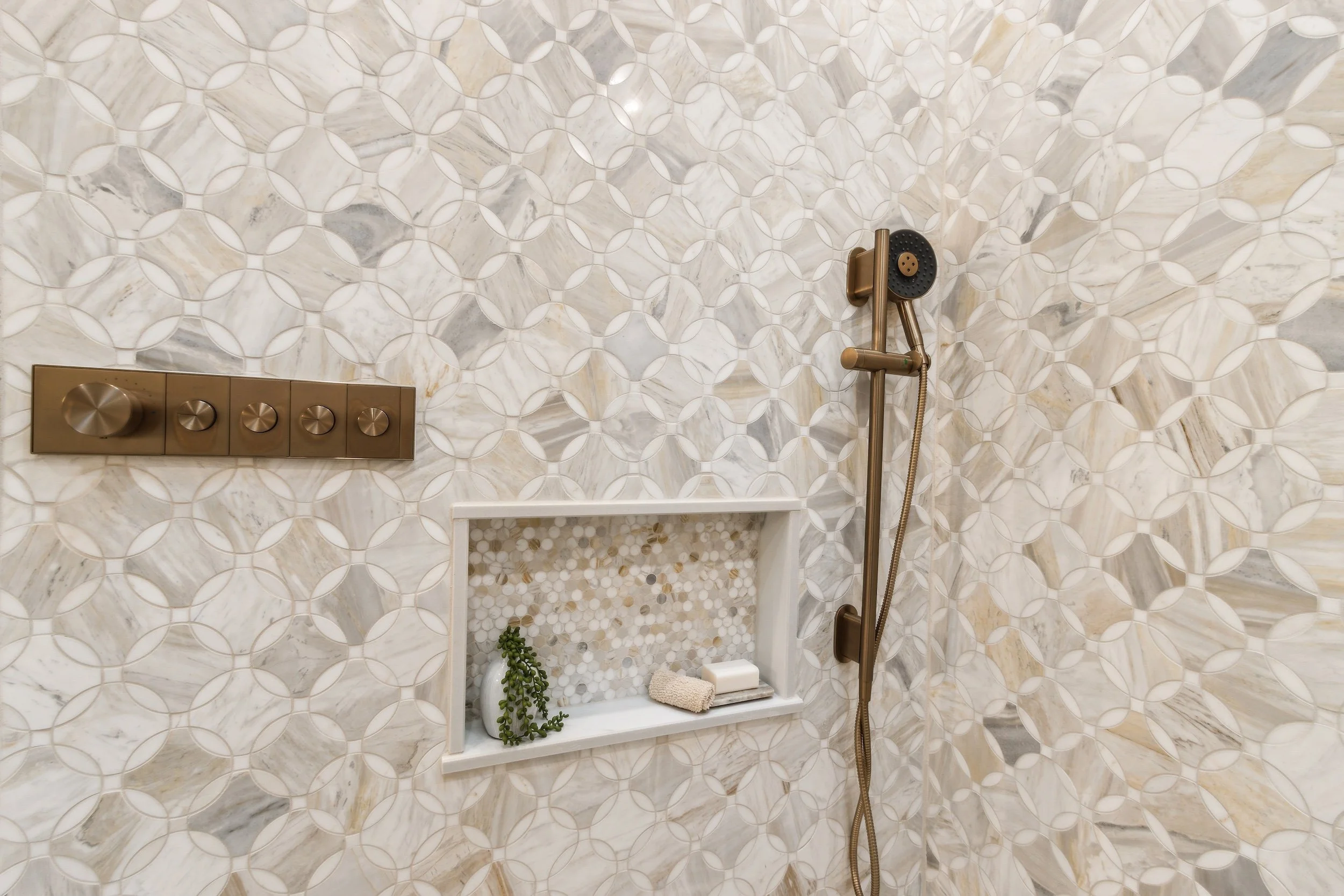 Shower wall with geometric patterned tiles, built-in niche with decor items, and bronze shower fixtures.