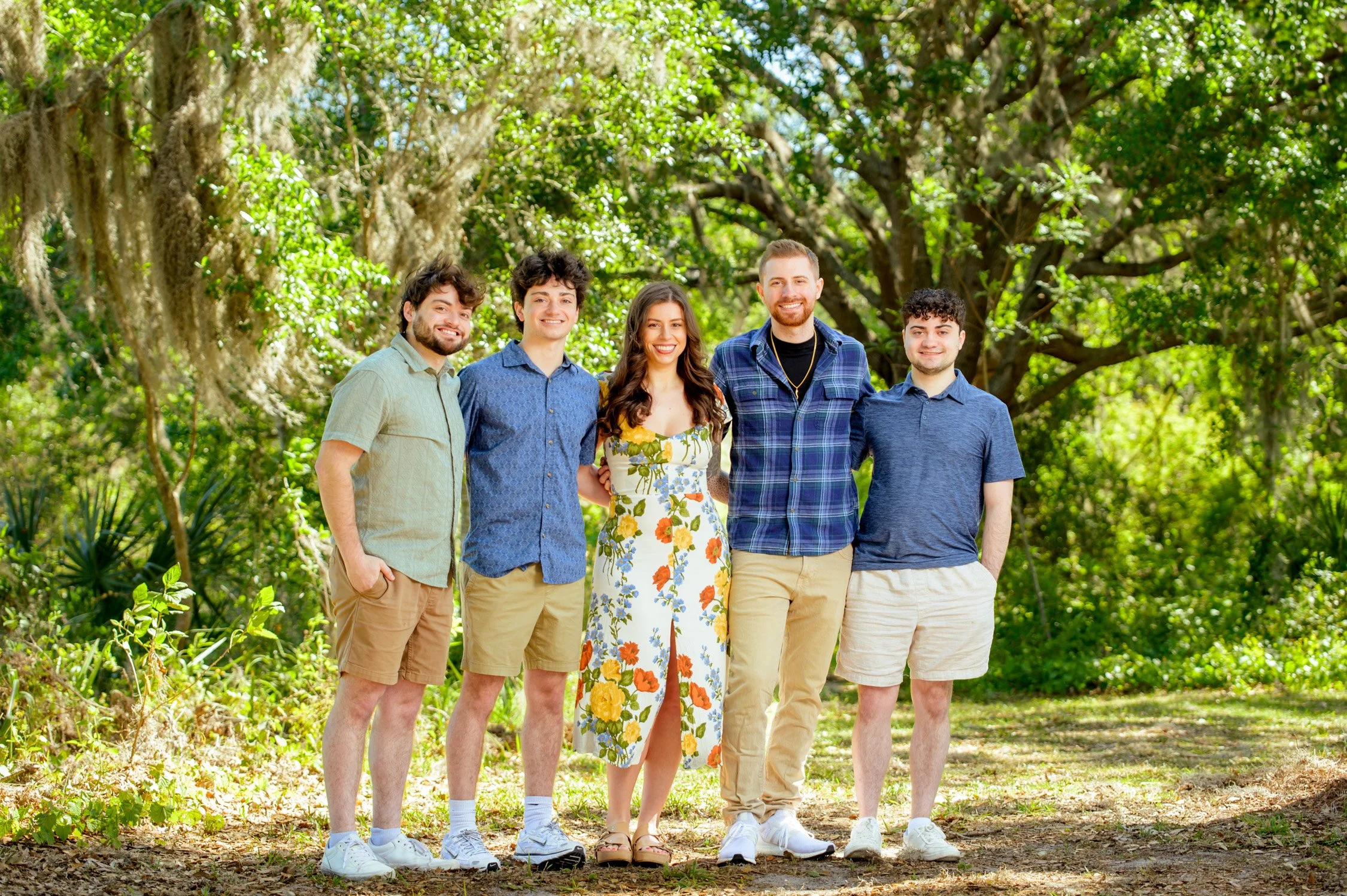 Group of five young adults standing outdoors in a green park, smiling for a photo.