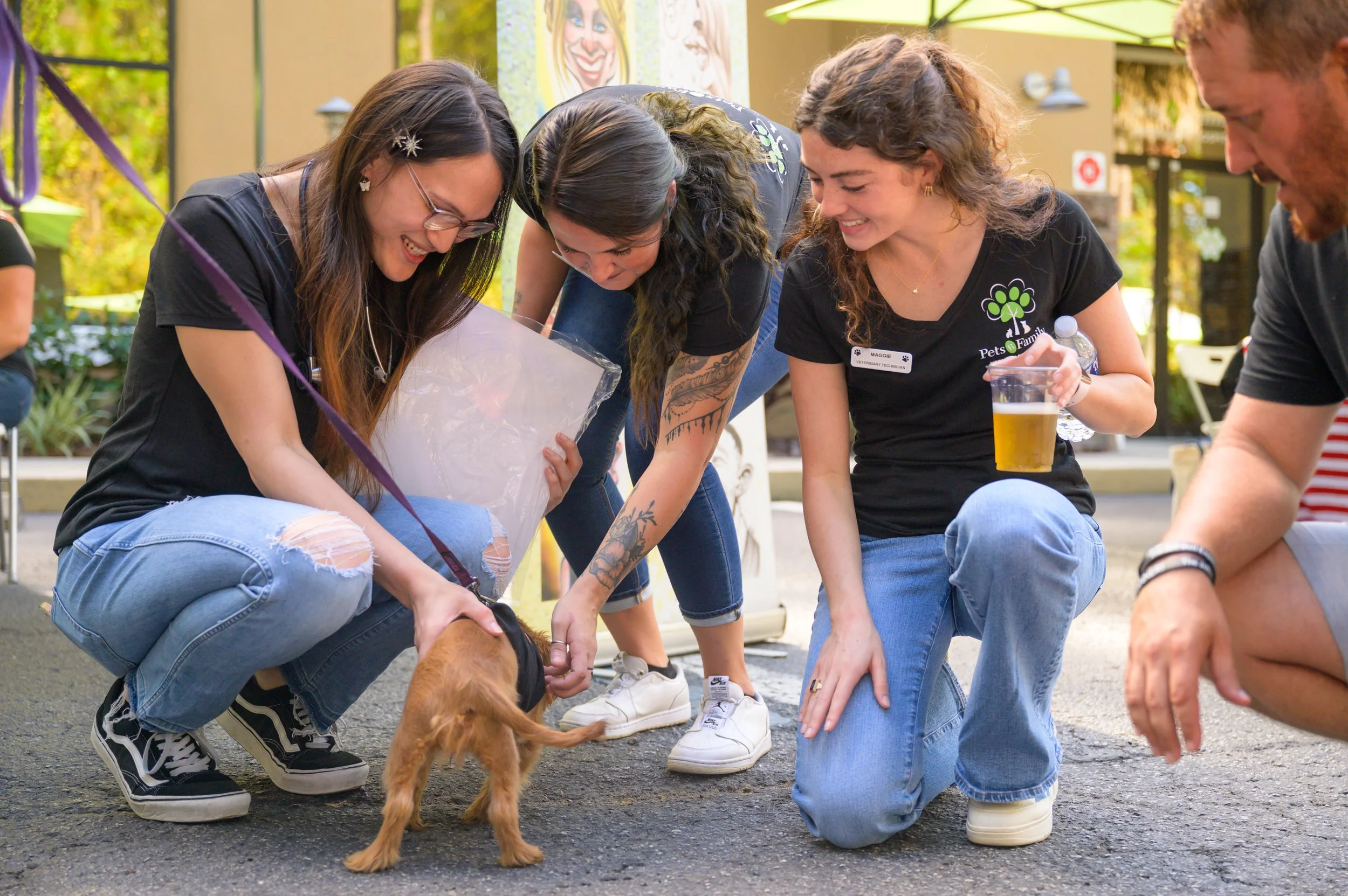 Four people and a puppy at an outdoor event, all smiling and interacting with the puppy on the ground.