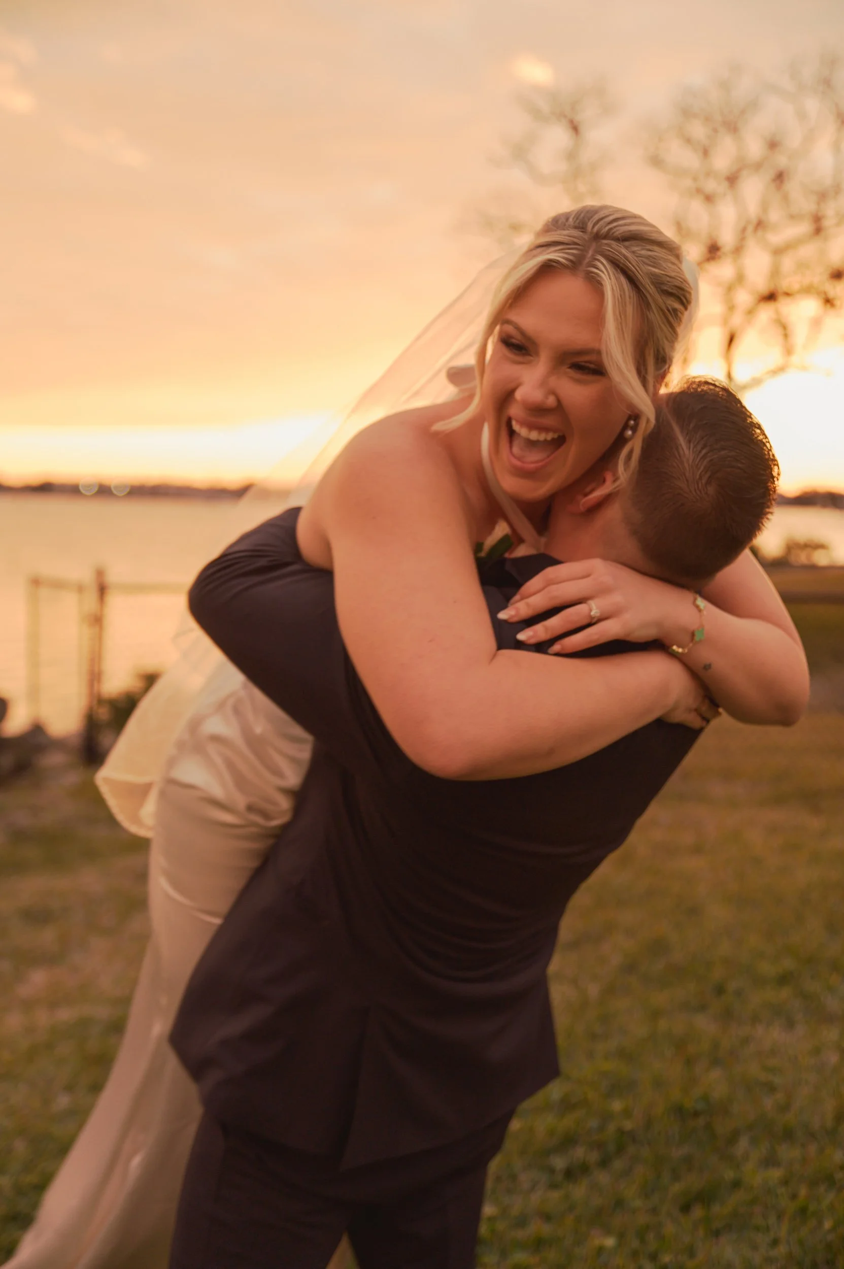 A joyful bride being lifted by her groom during sunset outdoors.