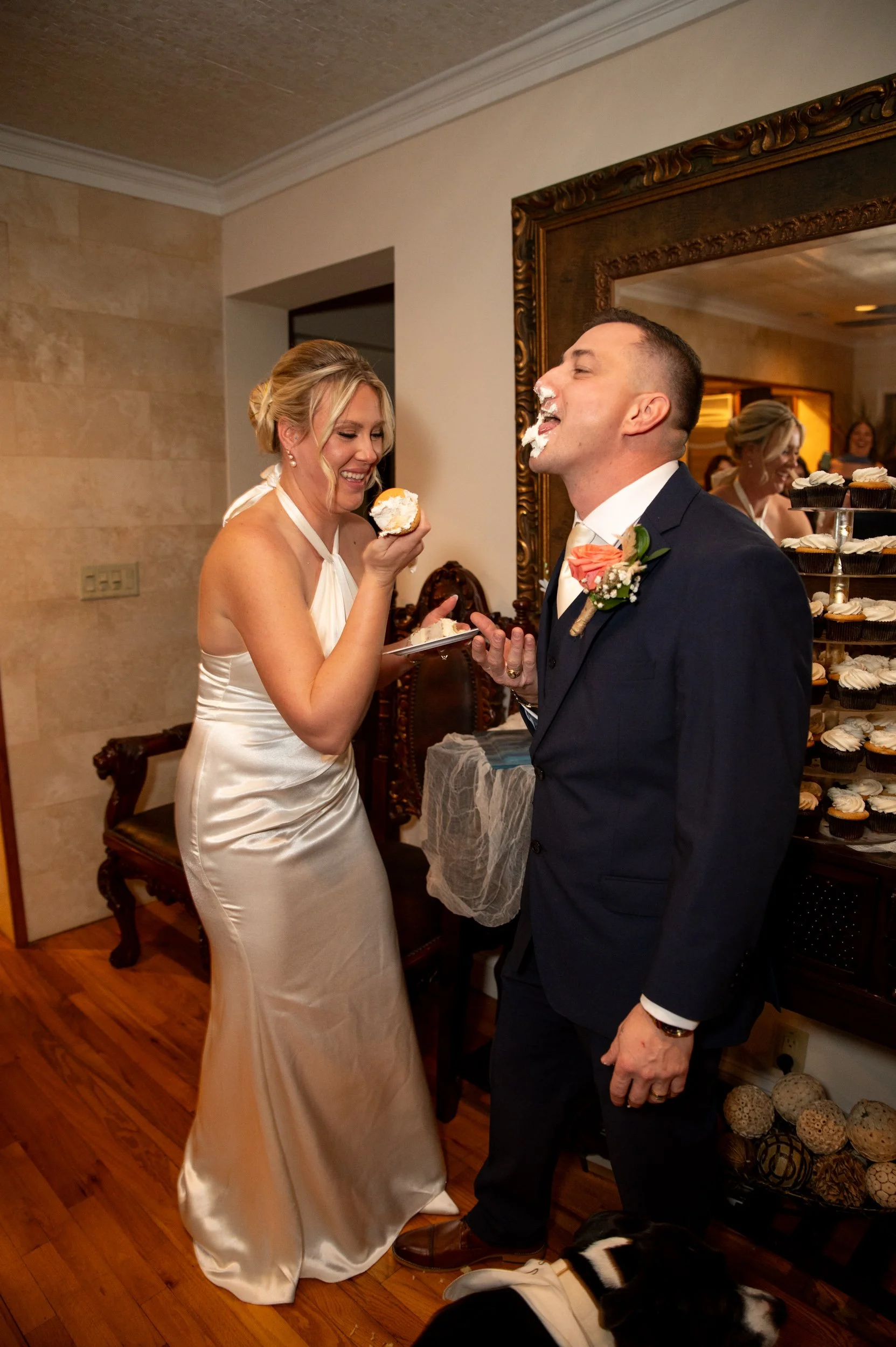 A bride and groom sharing a cake at their wedding celebration, with the bride feeding cake to the groom and both smiling.