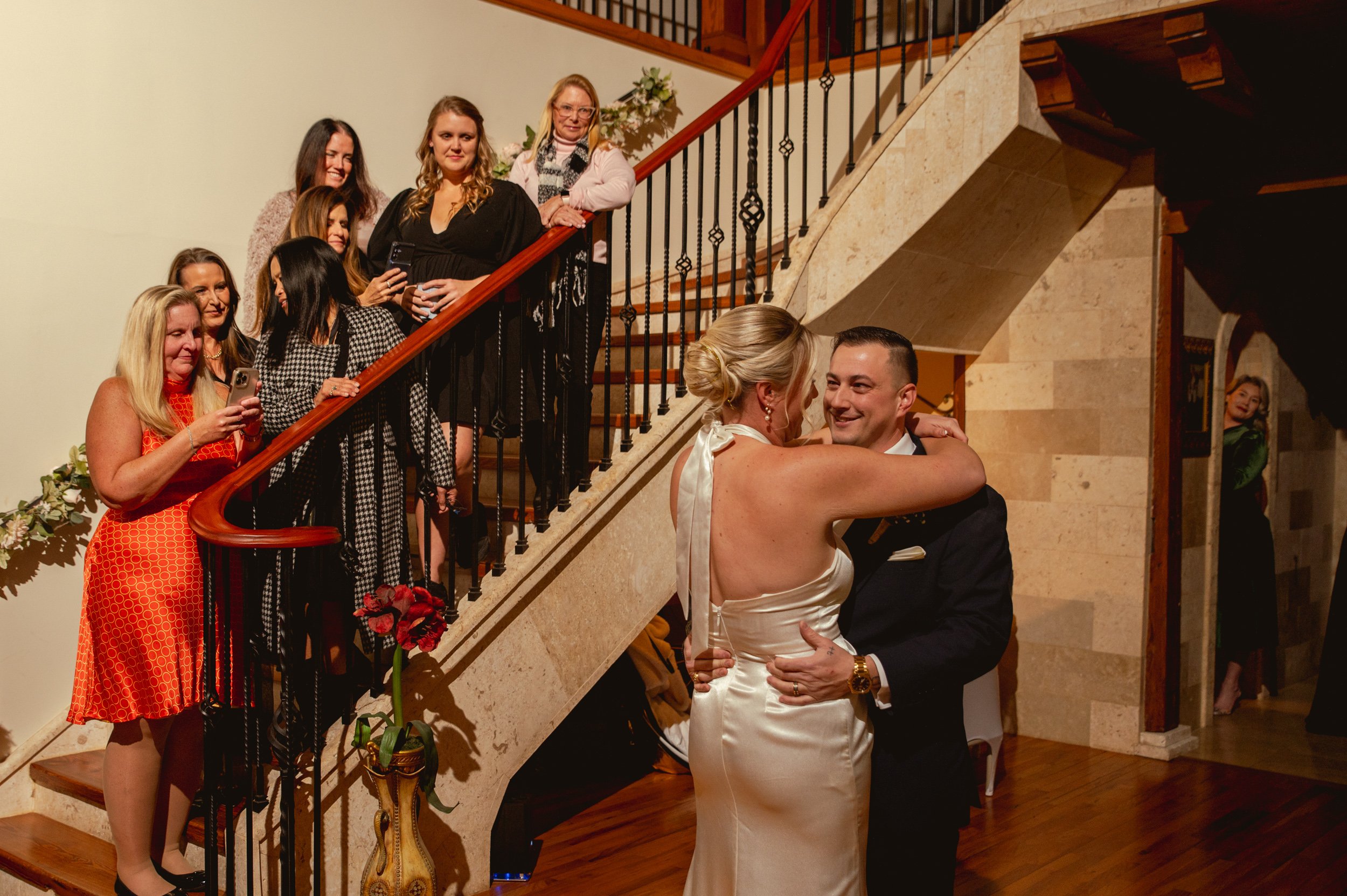 A bride and groom dancing in front of a group of women on a staircase during a wedding reception.