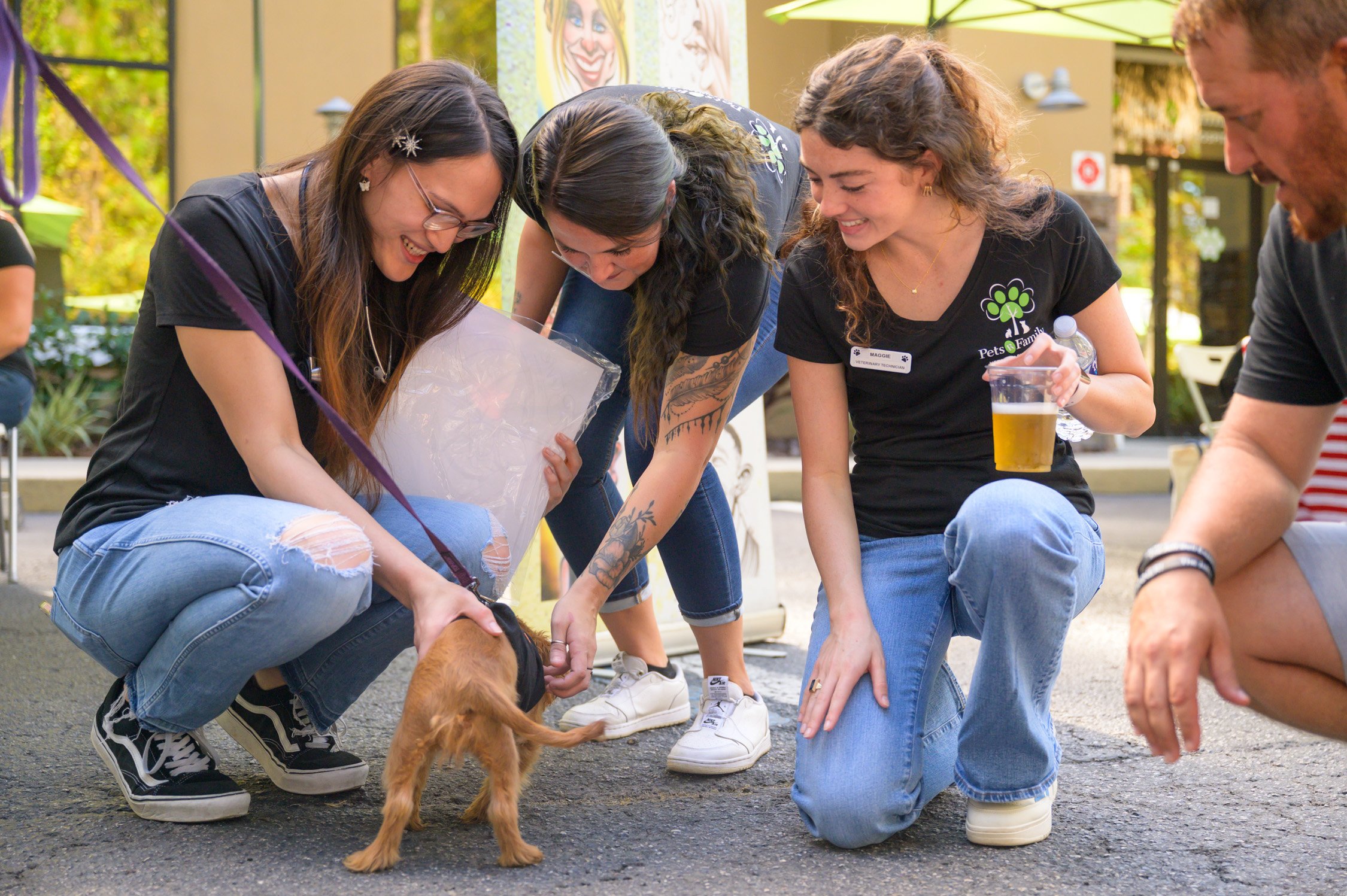 Group of people petting a small dog outdoors at a pet adoption event, smiling and interacting with the dog.