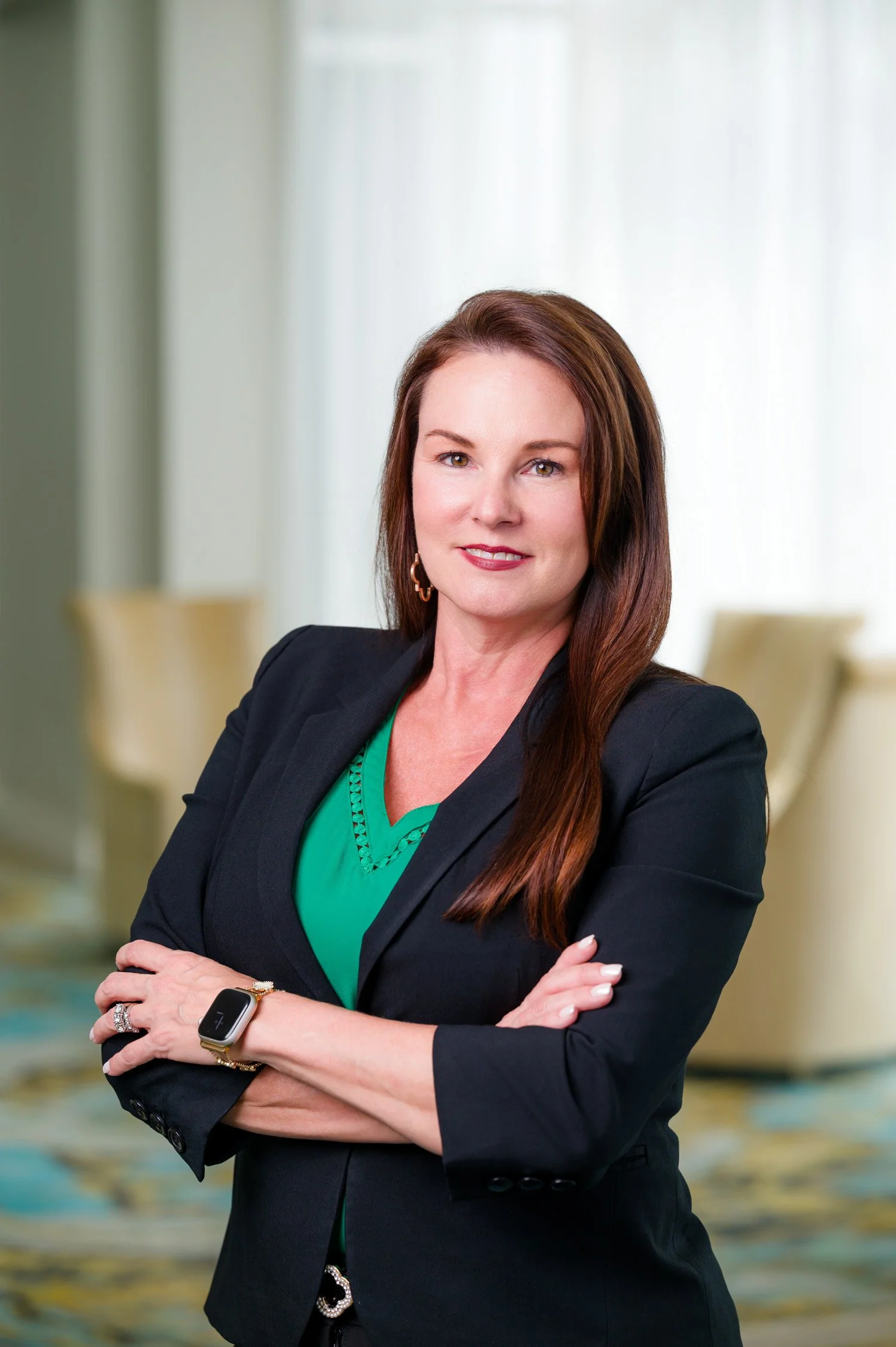 Businesswoman with brown hair and a black blazer posing with arms crossed in a professional setting.