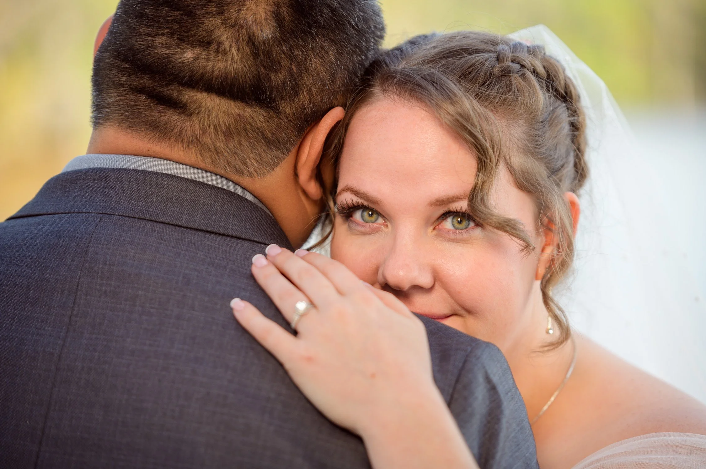 Close-up of a bride and groom holding each other during their wedding, with the bride's face visible and she is smiling and looking at the camera.