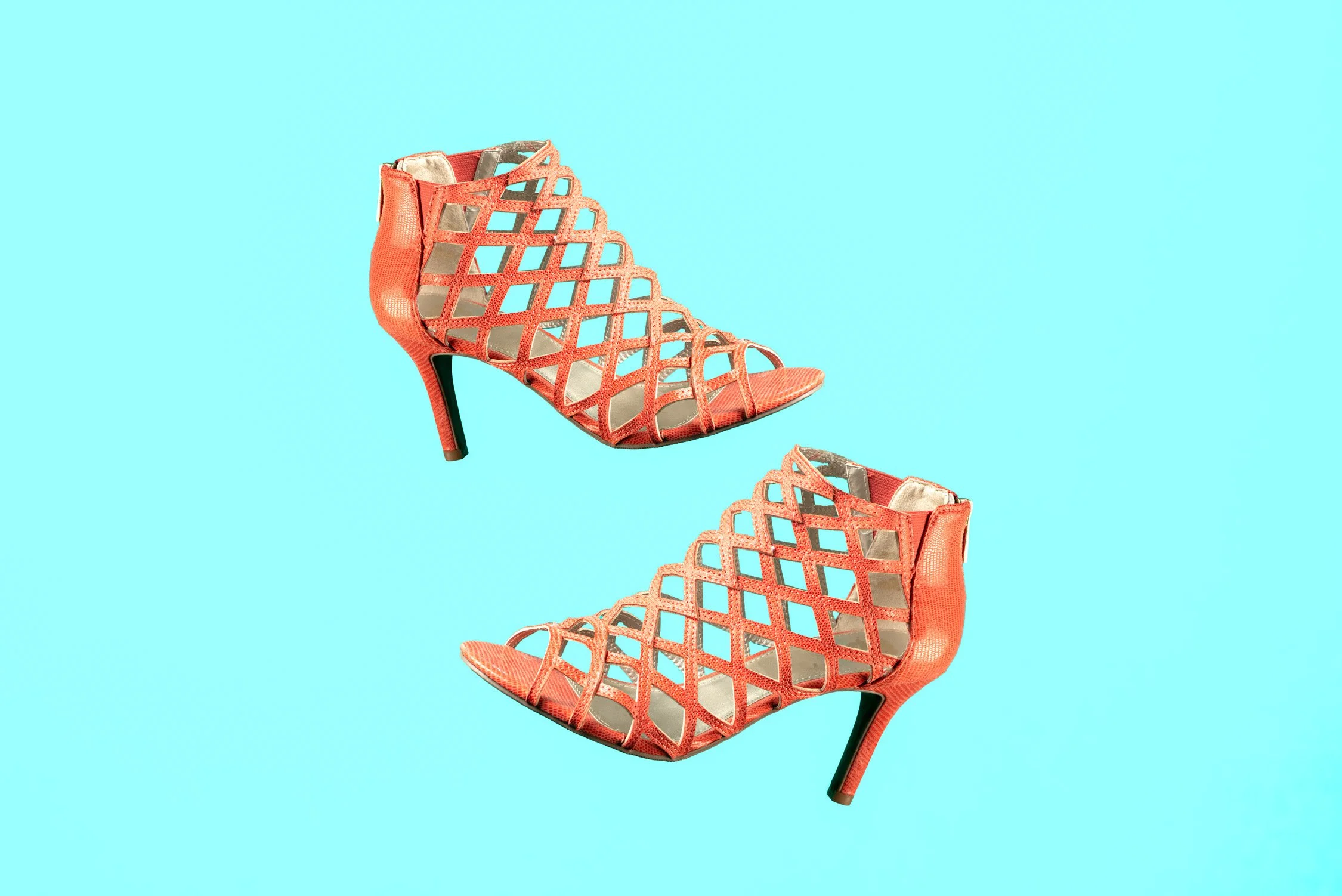 A pair of coral-colored high-heeled open-toe shoes with lattice design against a light blue background.