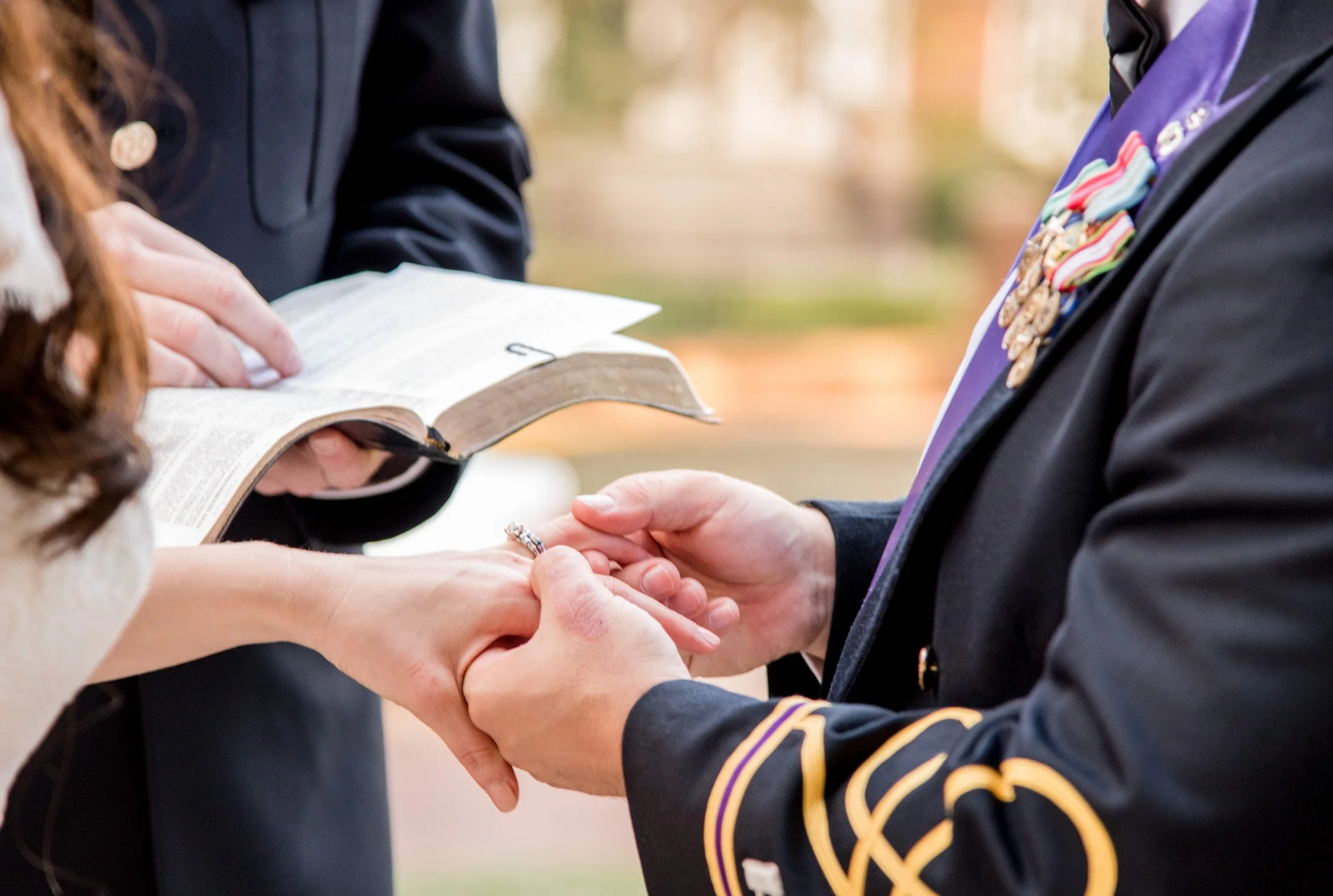A wedding ceremony where a groom is placing a wedding ring on a bride's finger, with an officiant holding a Bible nearby.