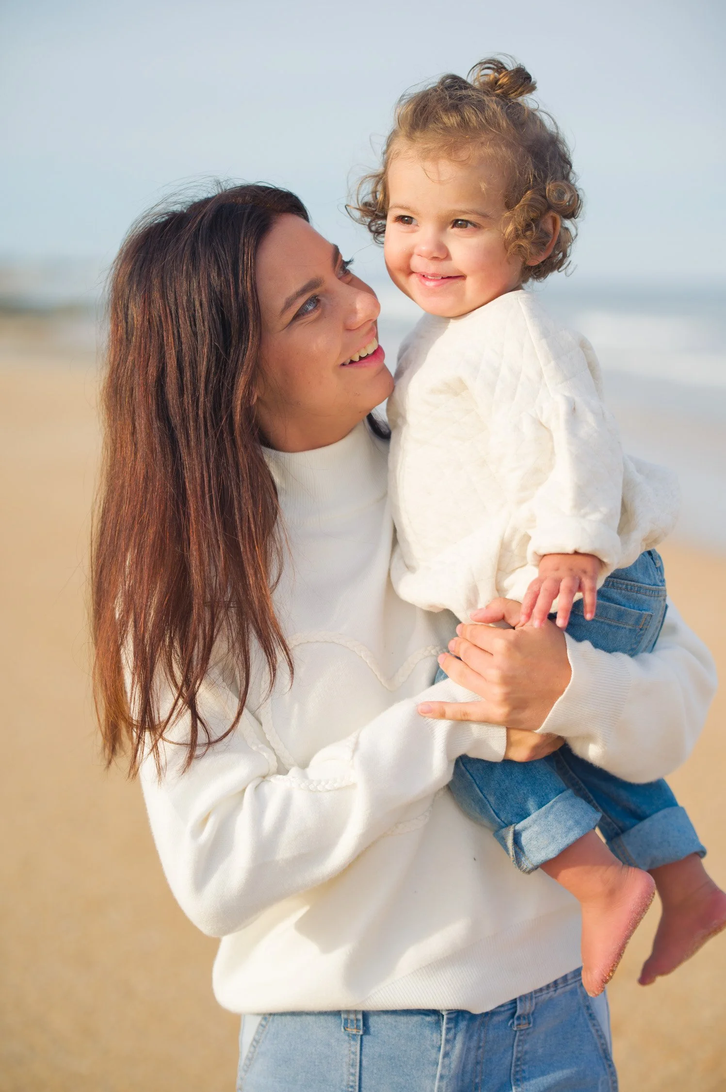 A smiling woman holding a young girl at the beach during daytime.
