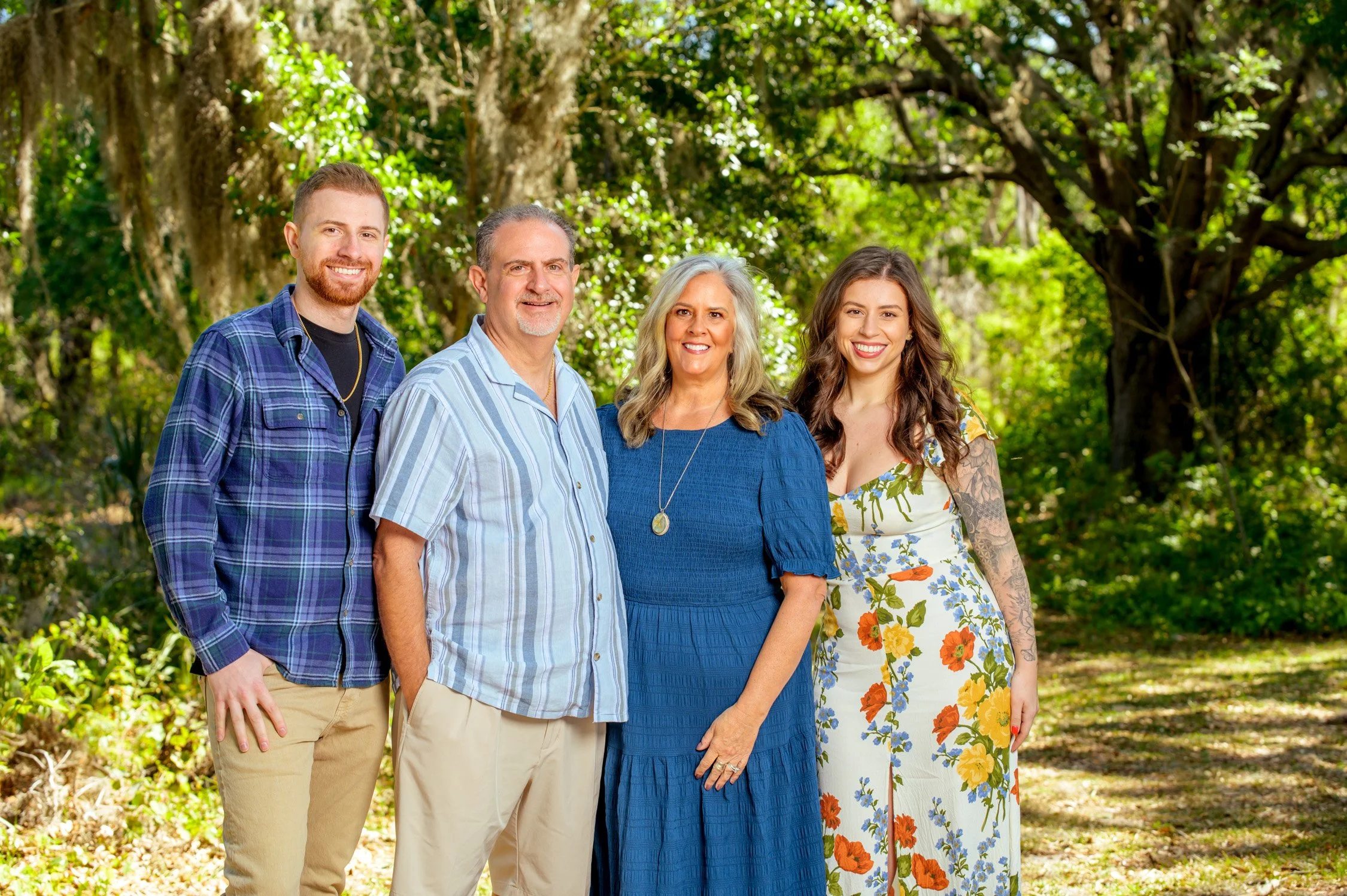 A family of five standing outdoors in a lush green park, smiling at the camera.