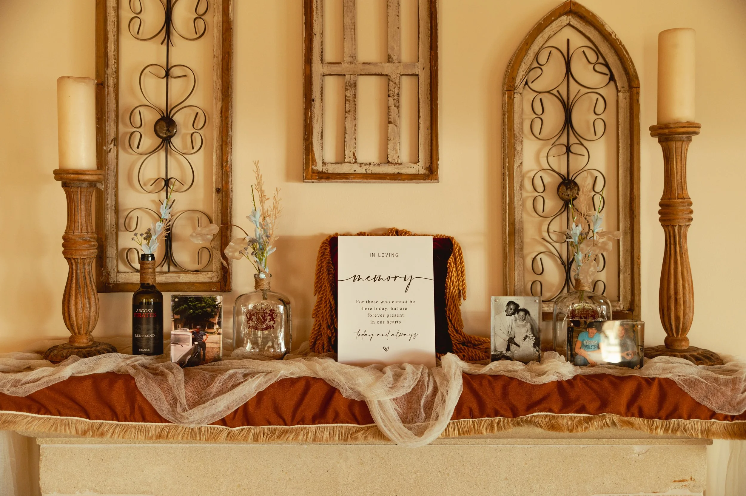 A memorial display on a shelf with candles, photos, a framed quote, and decorative elements, arranged against a warm yellow wall with ornate wall art.