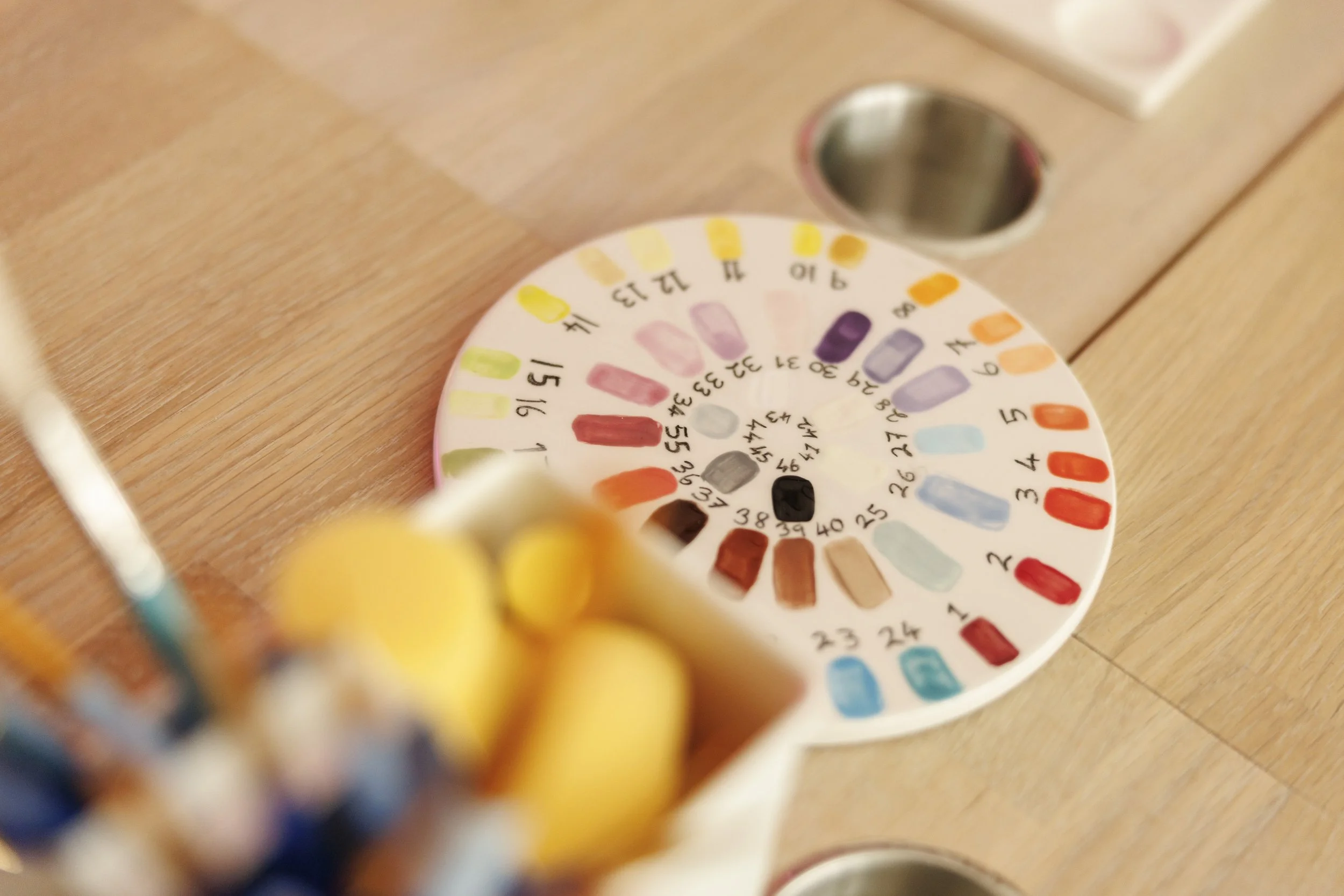 Close-up of a color-coded paint or marker color wheel, showing various shades and their corresponding numbers, on a wooden surface.