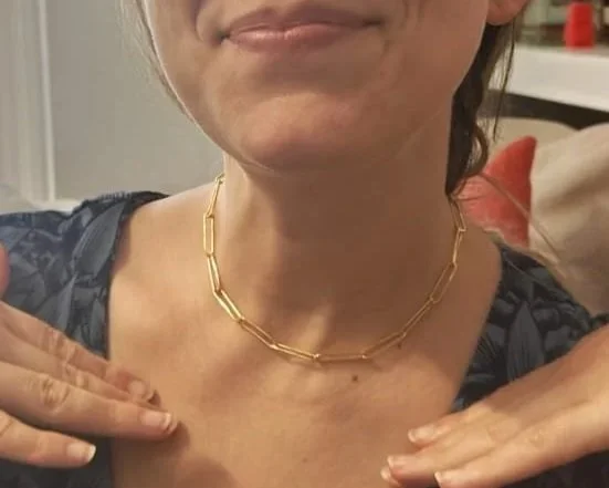 Woman wearing a gold chain necklace and making a 'peace' sign with her fingers.