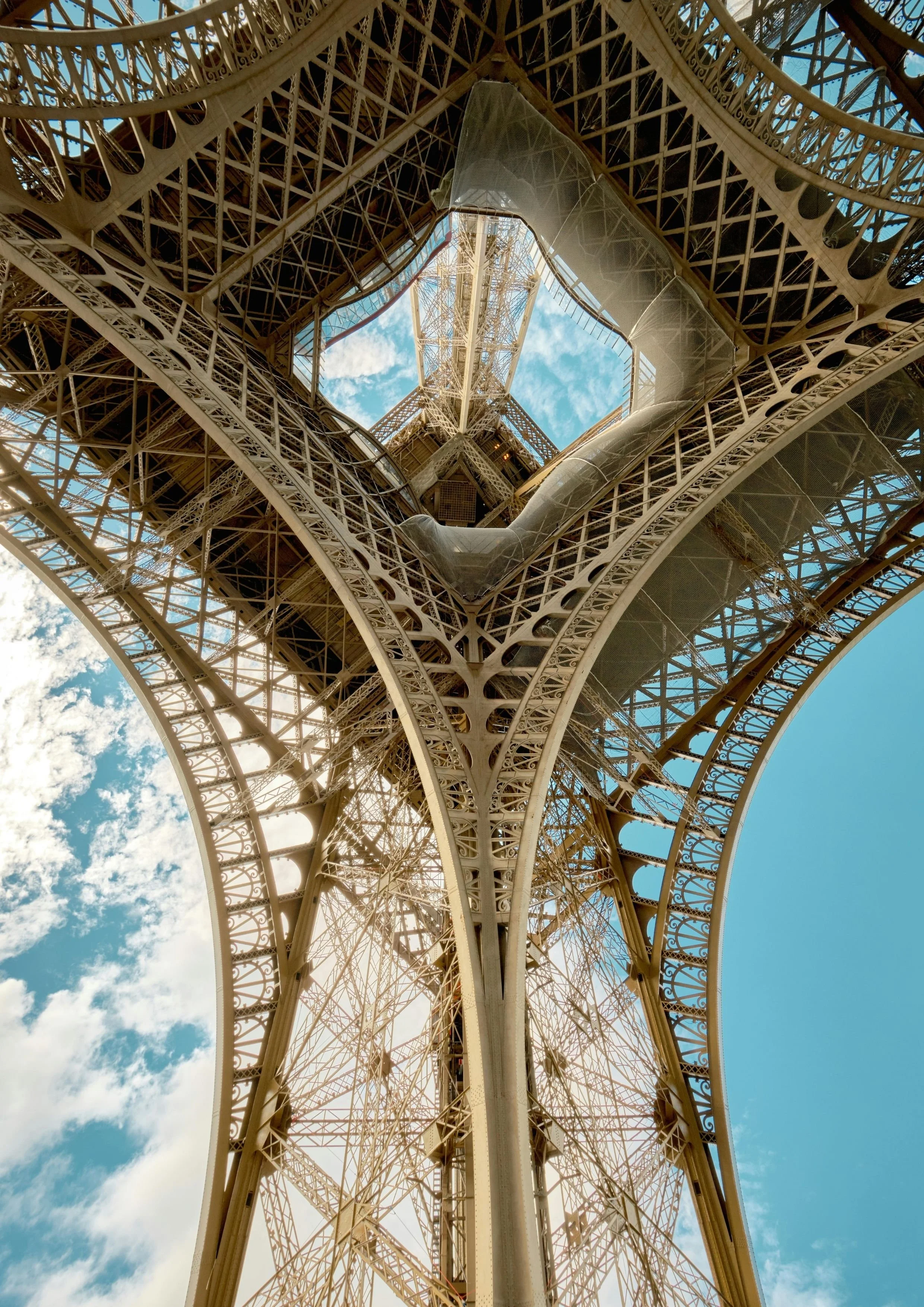 Vue ascendante de la structure métallique de la Tour Eiffel montrant le centre avec le ciel en arrière-plan.