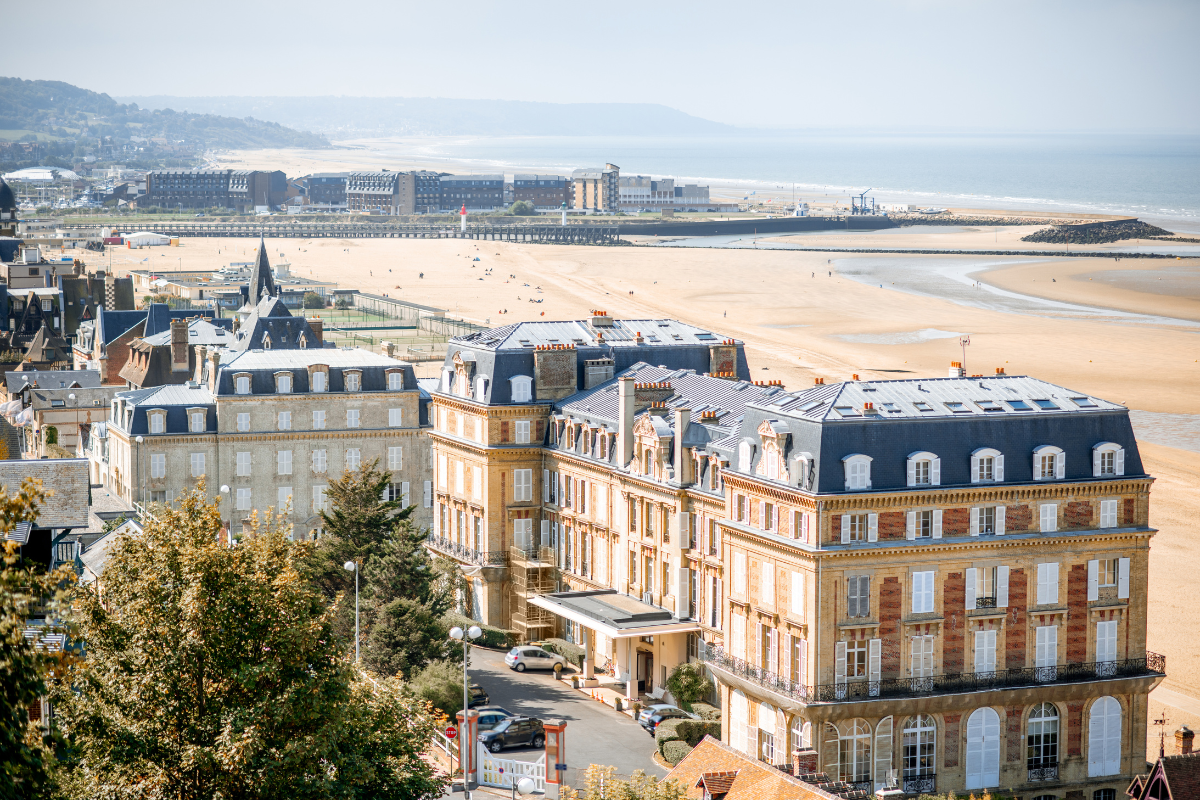 Coastal cityscape with historic buildings, a sandy beach, and ocean in the background.