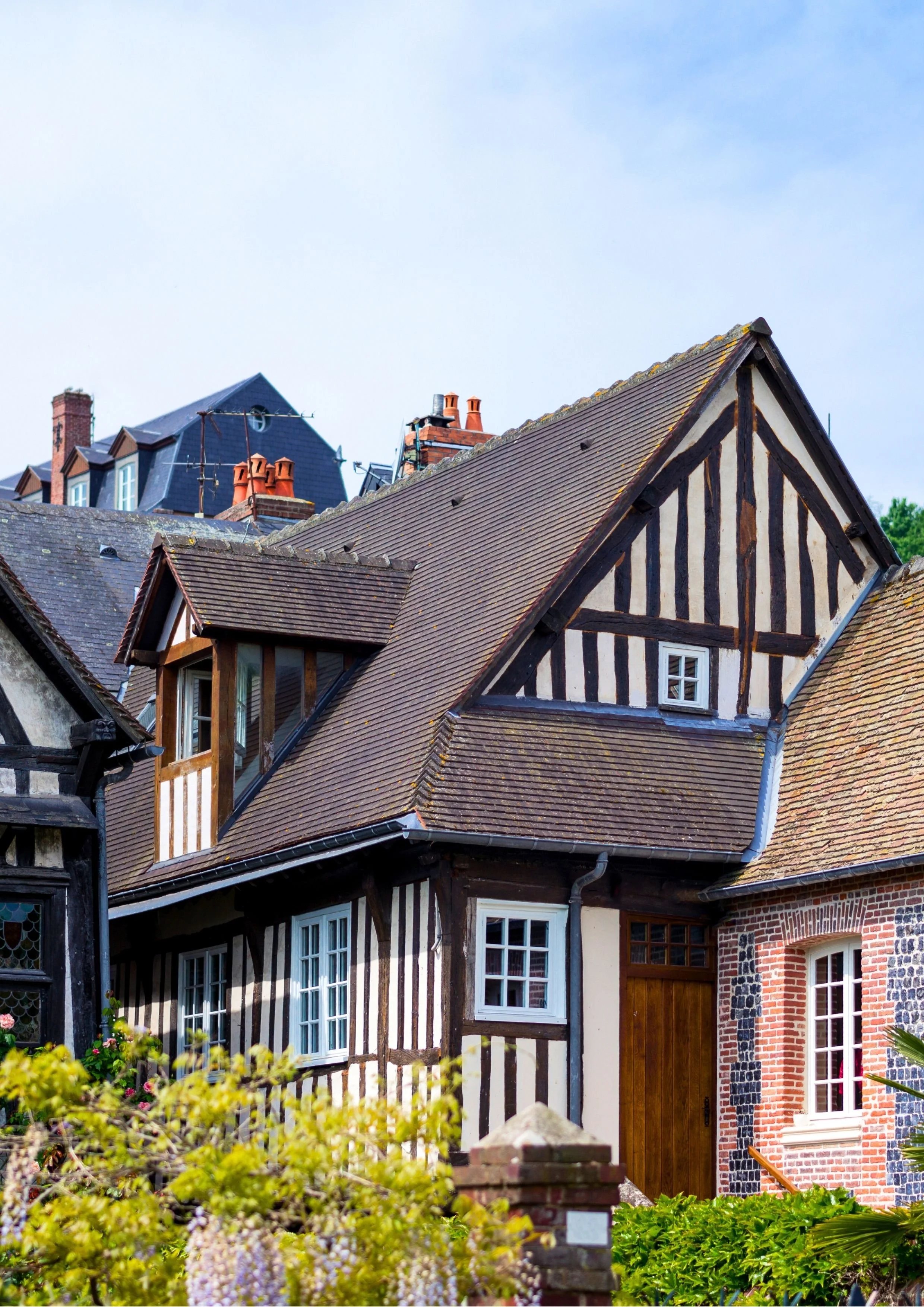 A traditional European-style house with a steep gabled roof, timber framing, and brick and stone walls, surrounded by greenery.