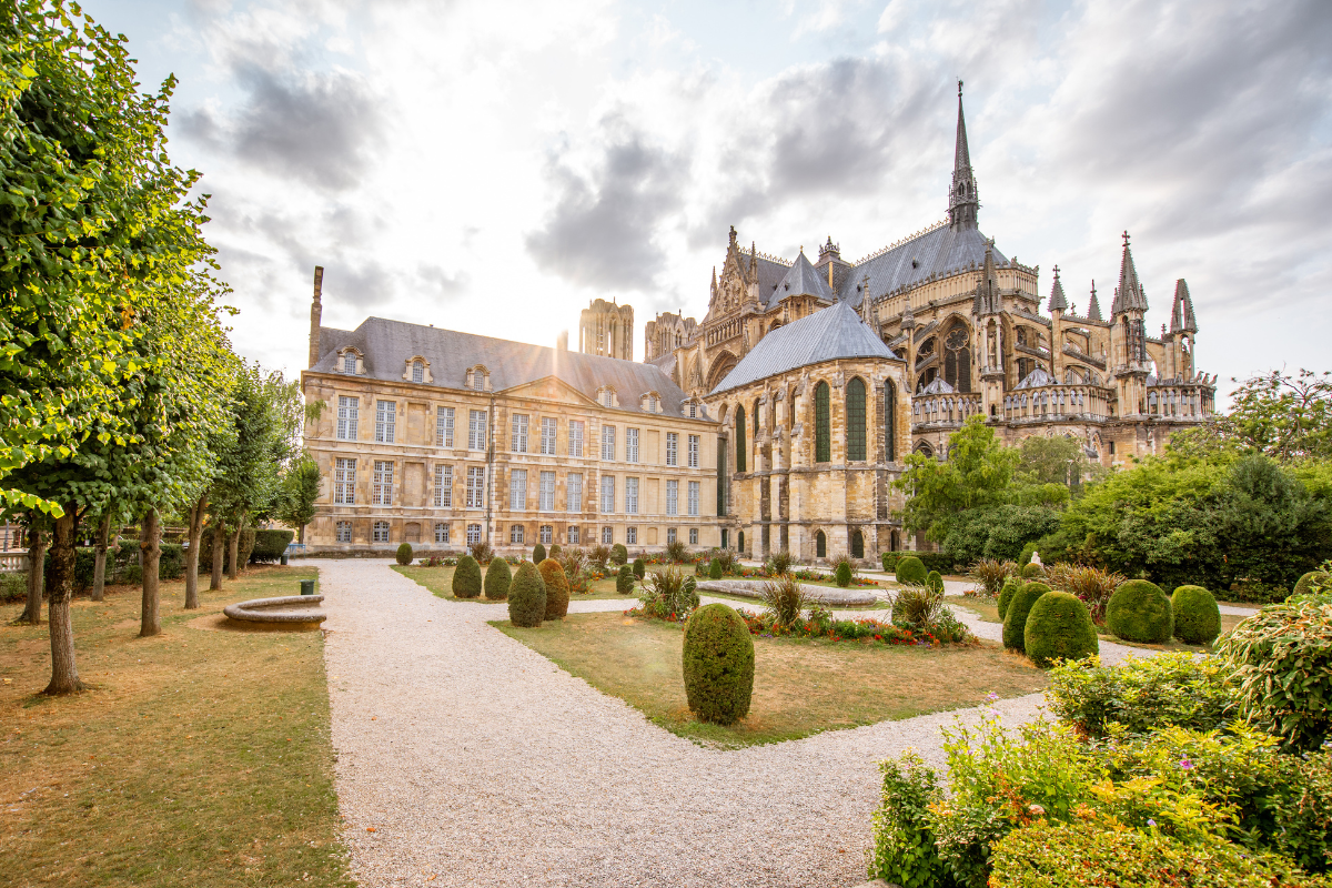 View of the Notre Dame Cathedral in Paris, France, with a garden path and landscaped greenery in the foreground under a partly cloudy sky.
