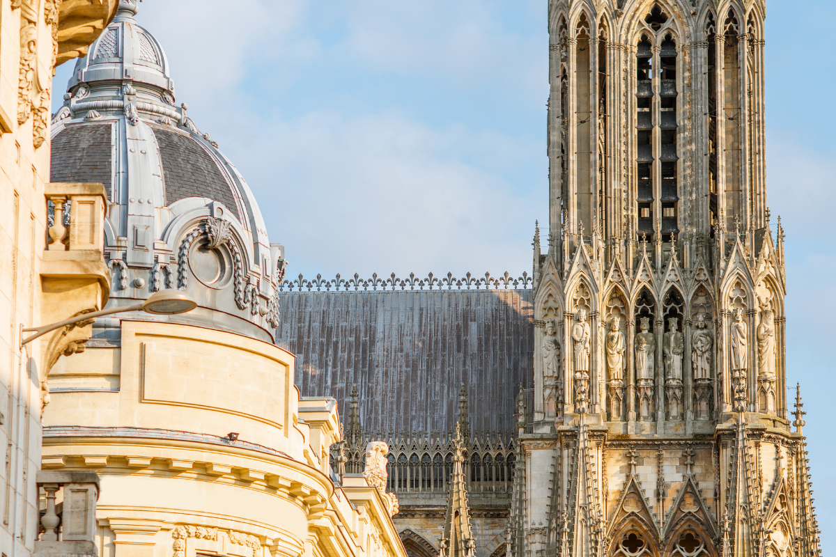Close-up of Gothic cathedral with ornate carvings and spires in sunlight, with a rounded building on the left.