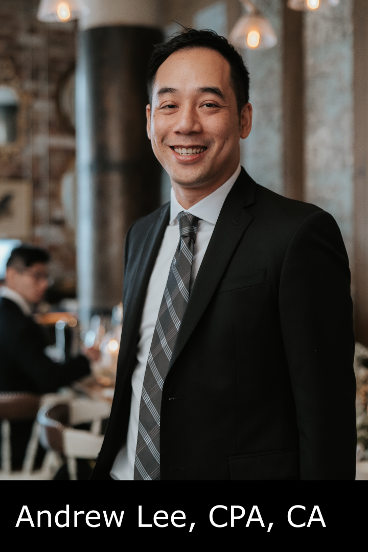 A man in a black suit with a white shirt and a gray plaid tie, smiling at the camera, in a warmly lit indoor setting with a rustic background.