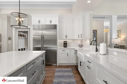 Modern kitchen with white cabinets, a large island with a white countertop, stainless steel appliances, and a hardwood floor.