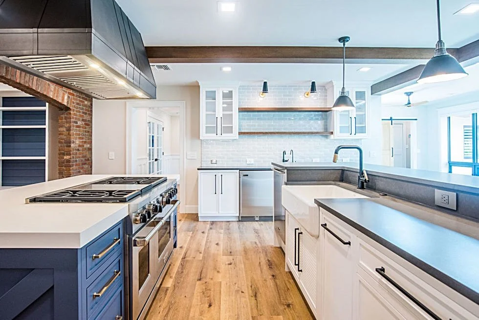 Modern kitchen with white cabinets, a large island with a farmhouse sink, stainless steel appliances, and pendant and recessed lighting.
