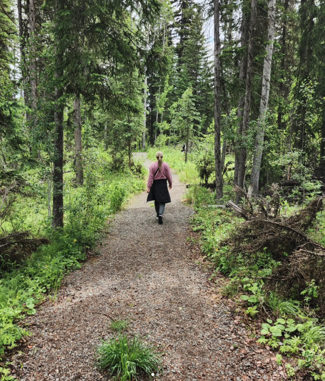 A person walking on a dirt trail through a dense green forest.
