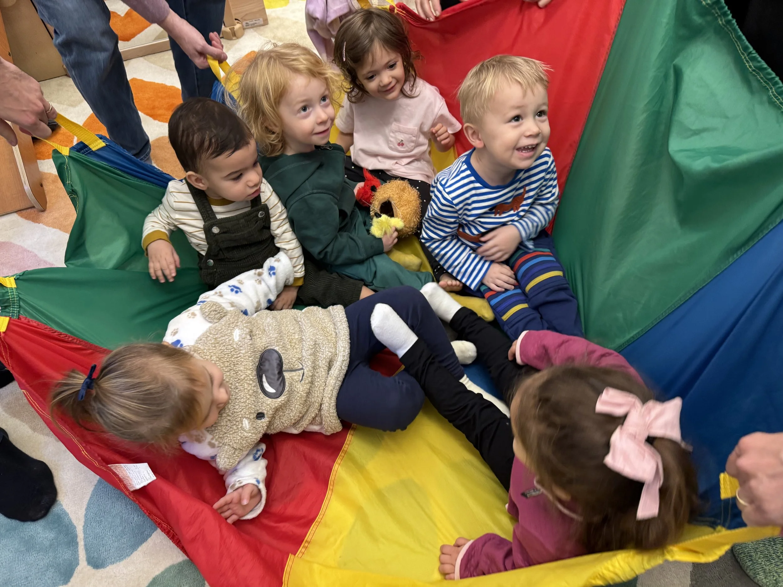group of six young children in a parachatue carousel during a mommy  and me class