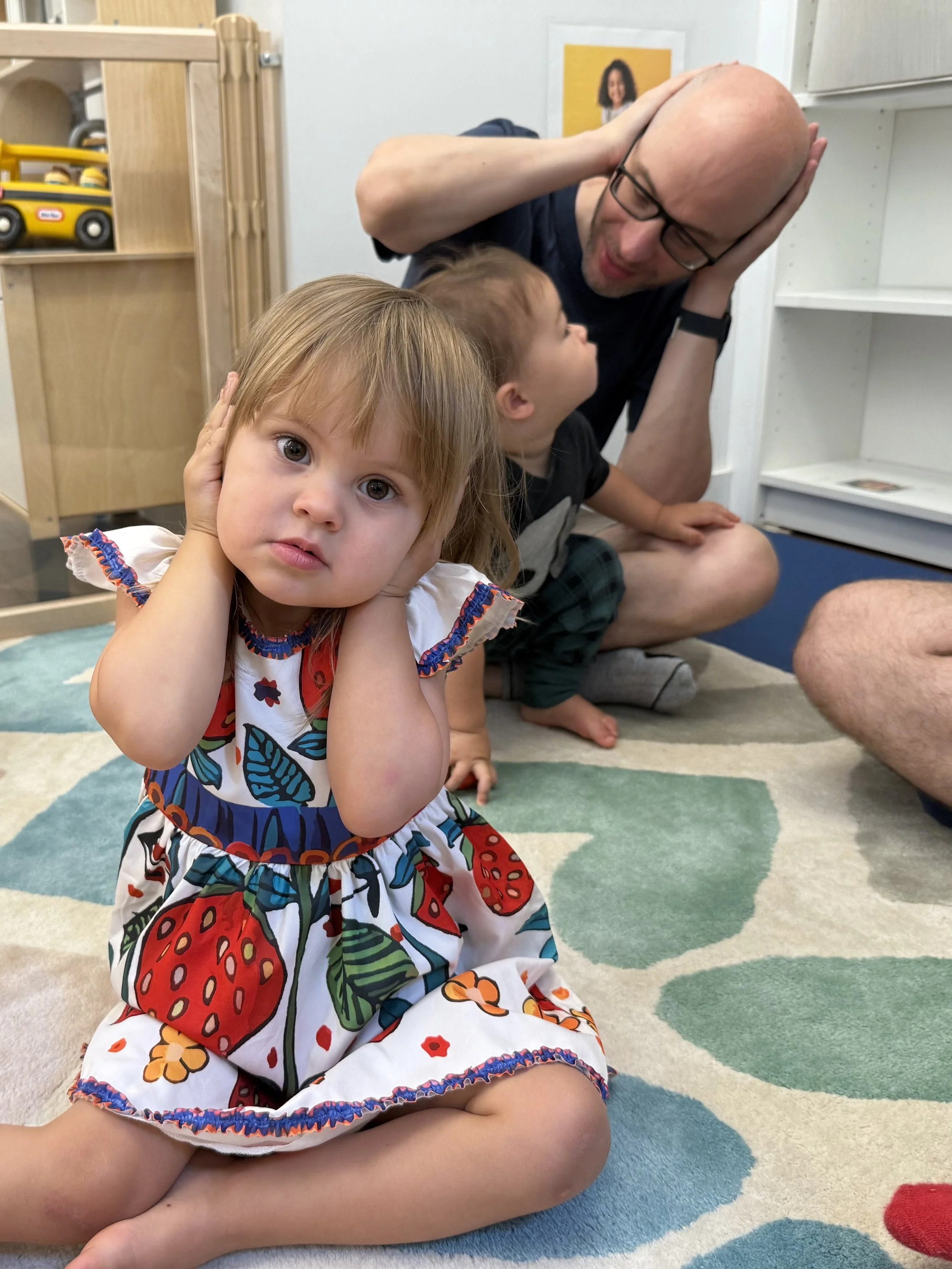 young girl singing and doing body movements, behind her a dad with his young son participating too