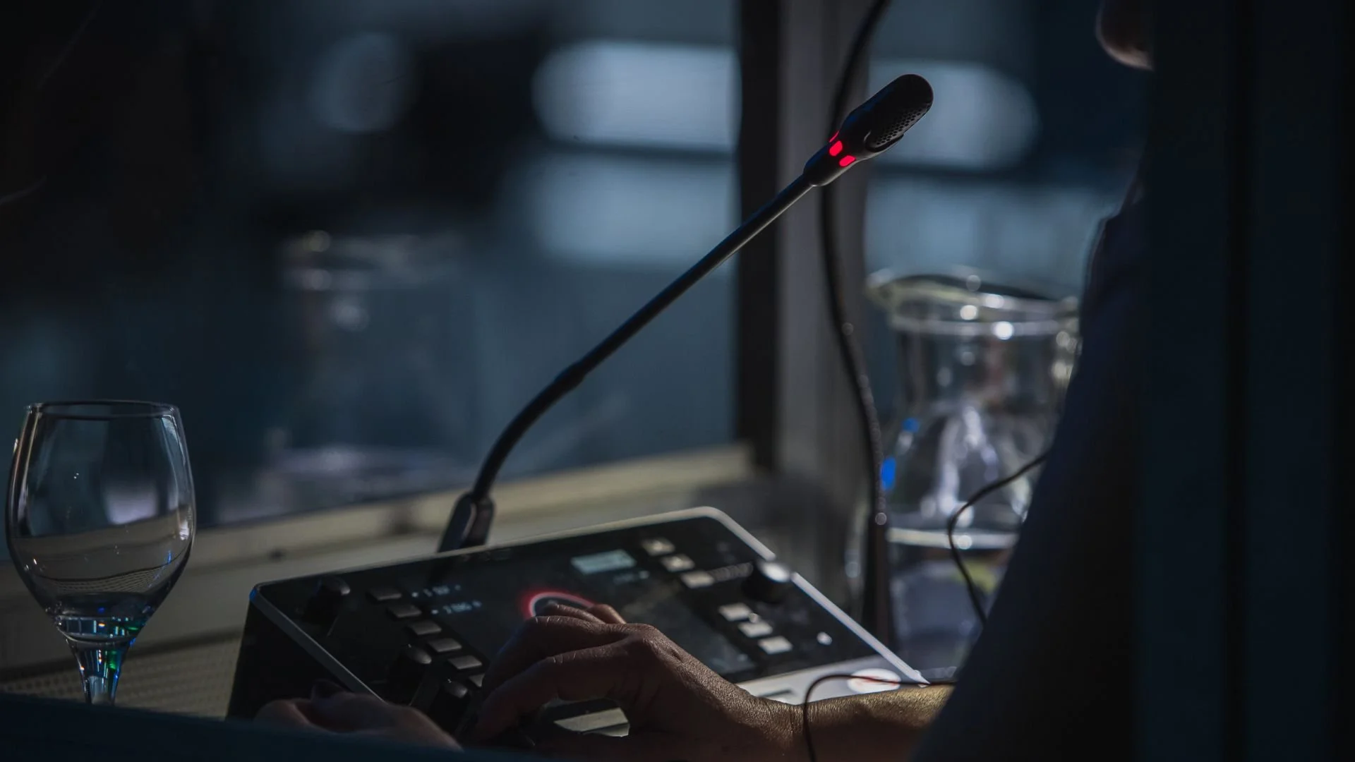Nahaufnahme eines Dolmetschermikrofons in einer Übersetzerkabine. Am Mikrofon leuchtet ein rotes Licht, dass Aktivität signalisiert