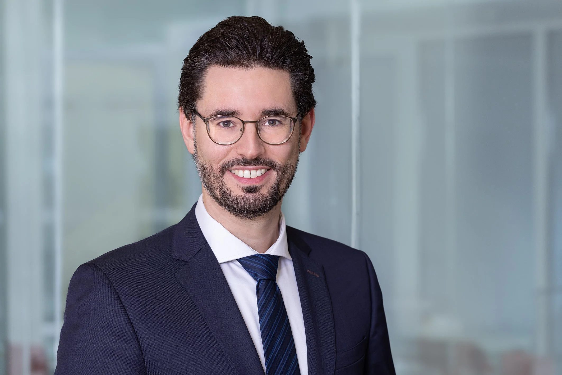 A representative picture of the CEO, Dr. Christian Schütz. He has a trimmed beard wearing a suit and tie, smiling in a modern office setting.
