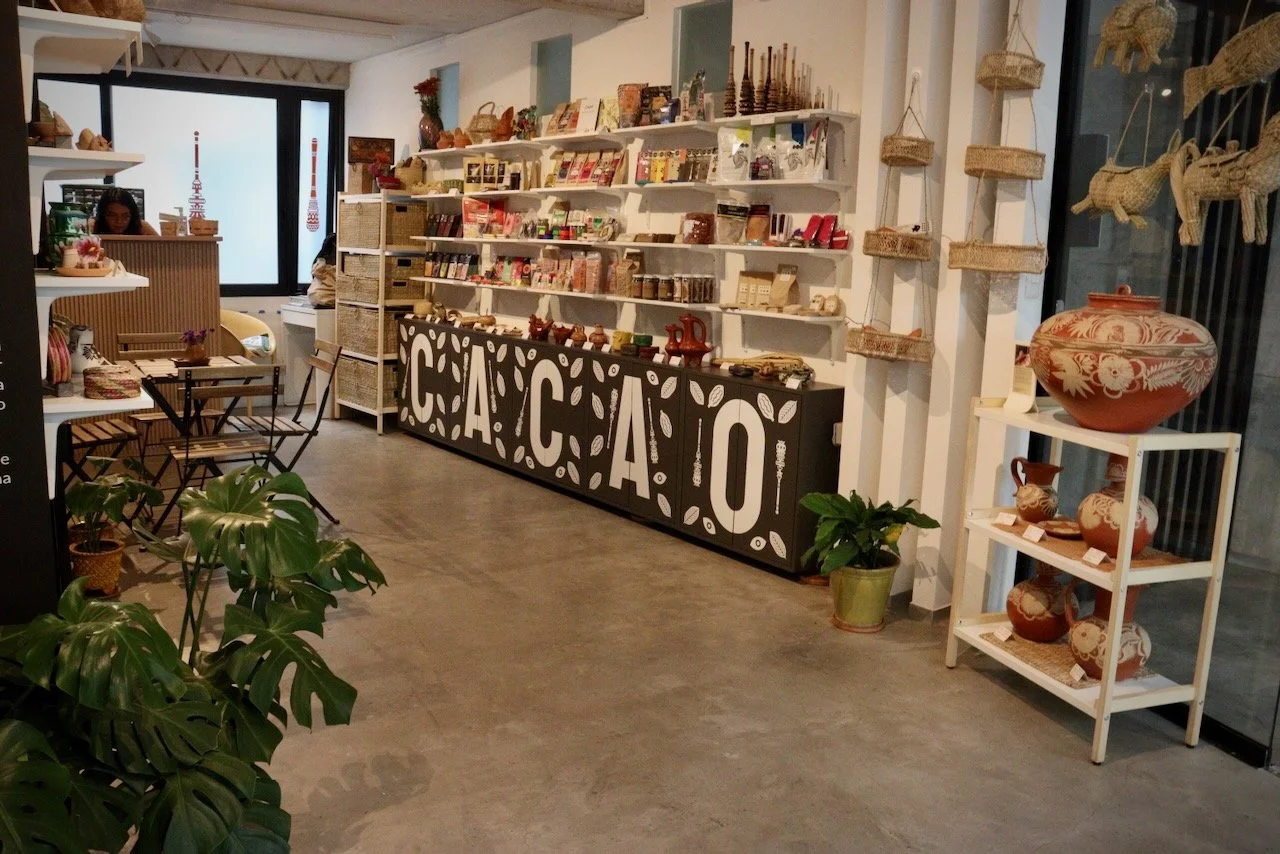 Interior de una tienda de artículos artesanales con estanterías llenas de cerámicas, pandas con plantas y una caja grande con letras que dice 'CA' en color negro y blanco.