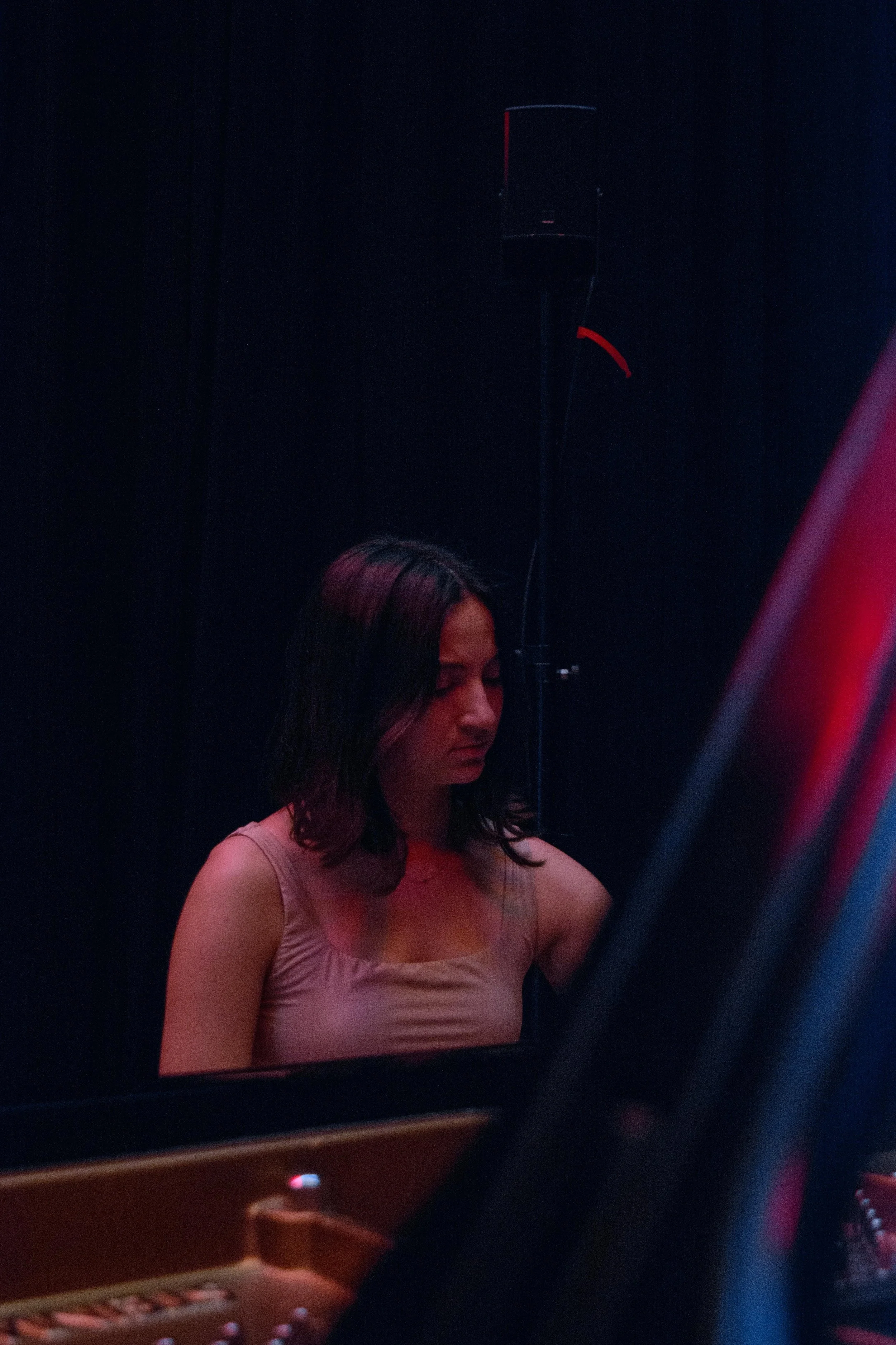 A woman with dark hair sitting at a piano with her eyes closed, in a dimly lit room.