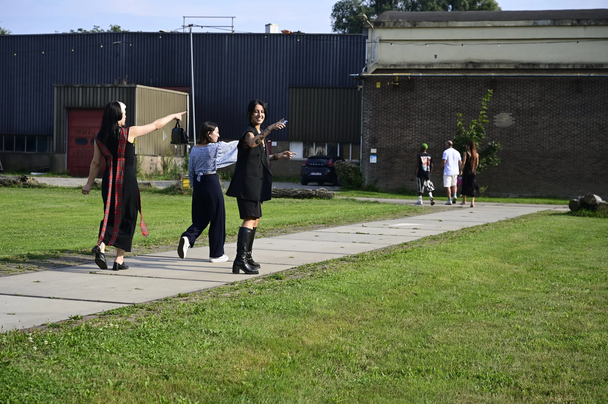 Four women walking on a sidewalk in an urban area, with three women in the foreground smiling and one woman in the background walking away from the camera.