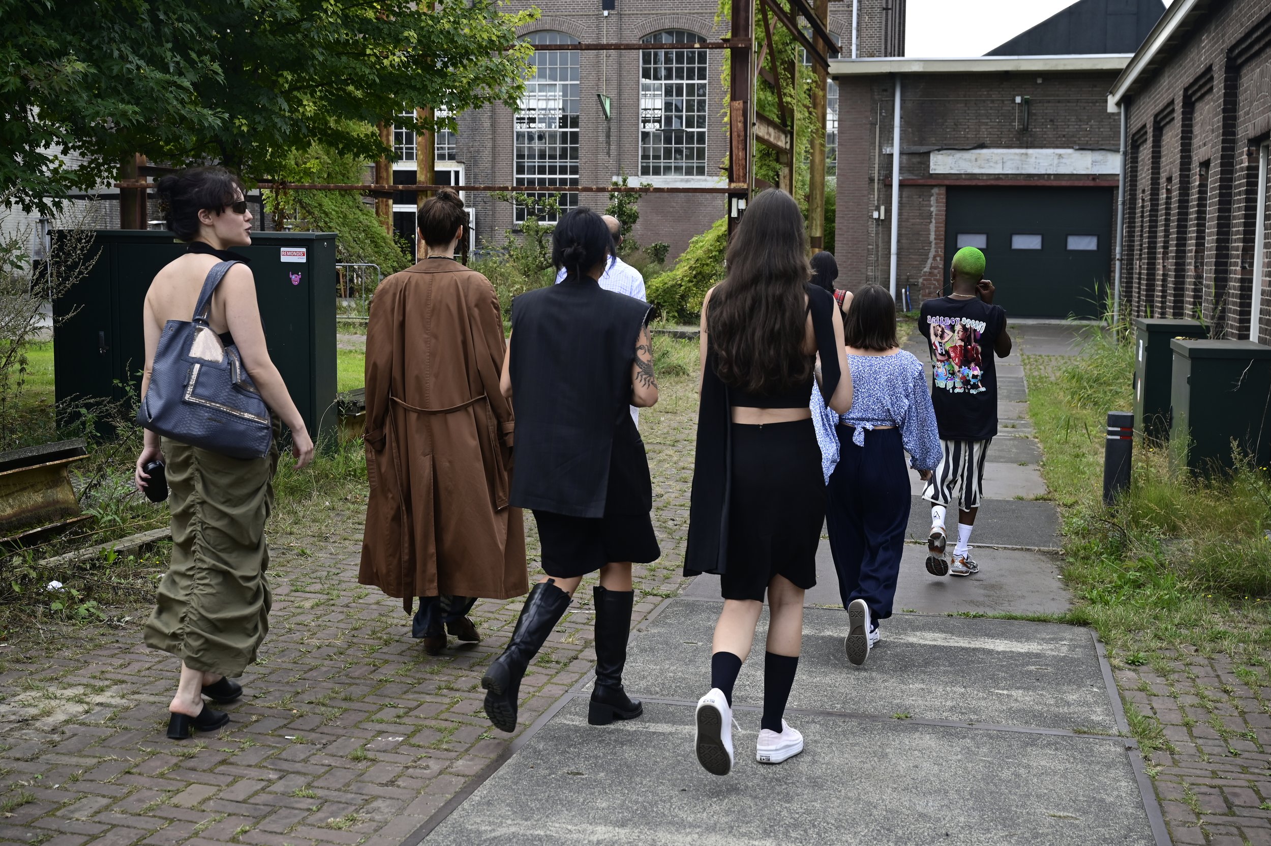 A group of diverse people walking away on a sidewalk in an urban area with brick buildings and greenery.