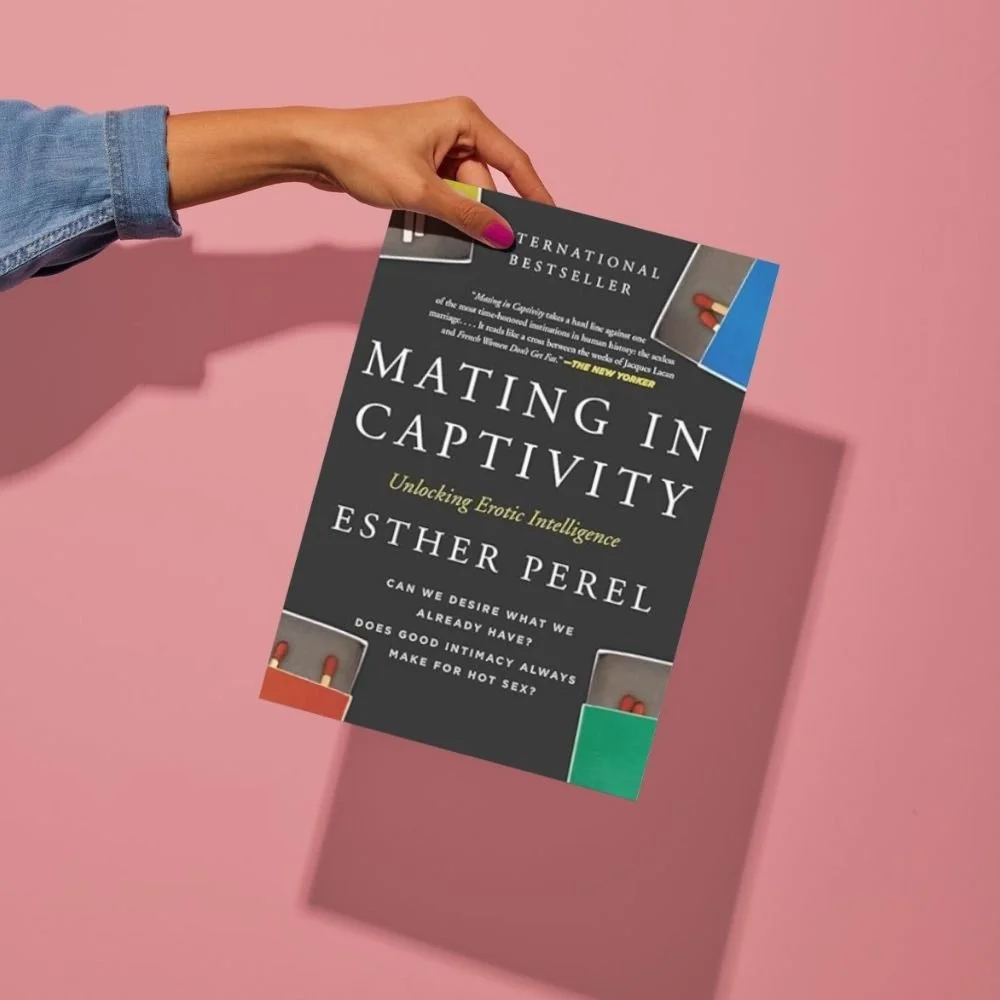 A person holds Mating in Captivity by Esther Perel over a pink background