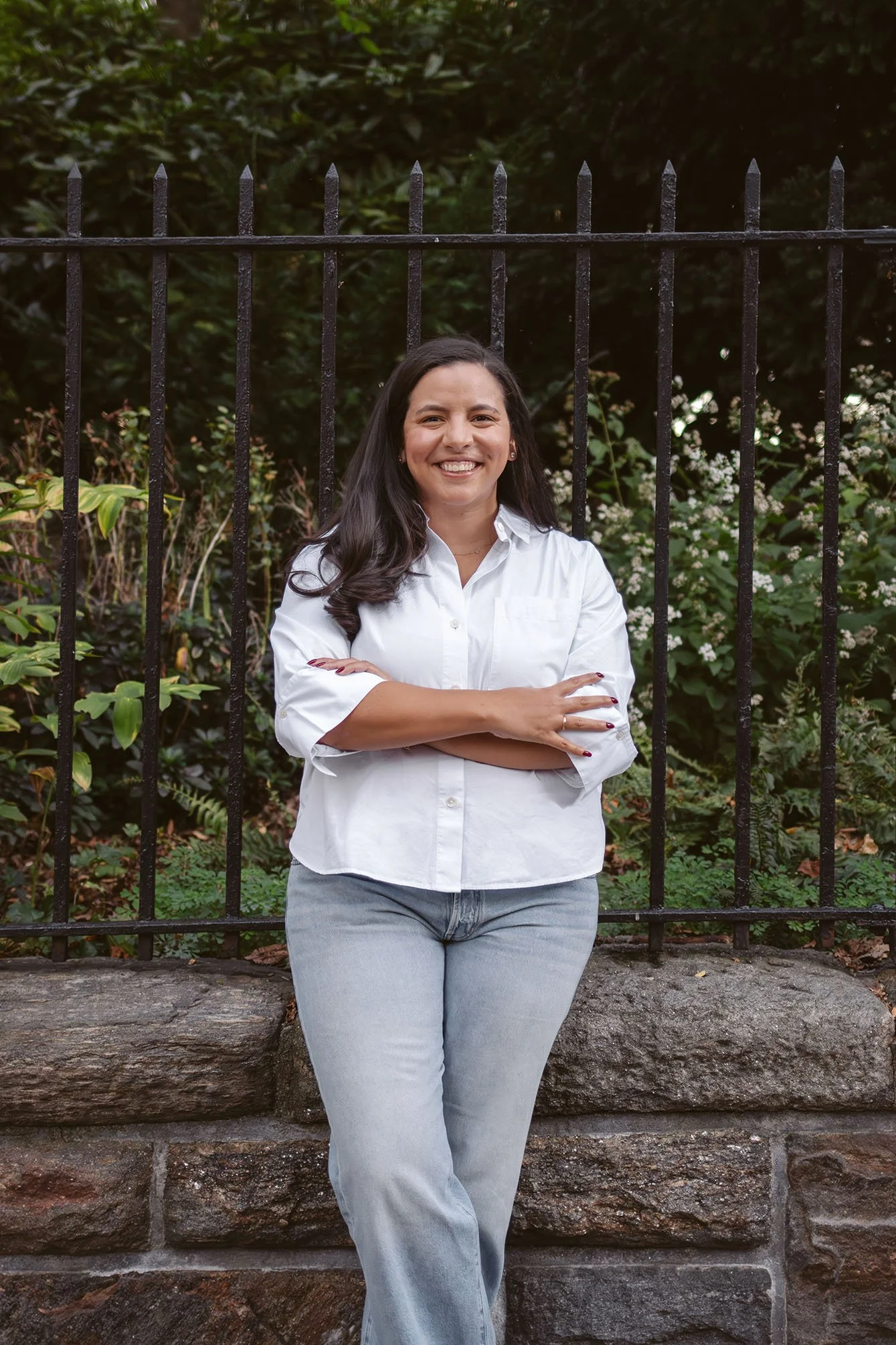 Jessica leans up against an outdoor wall, arms crossed and smiling