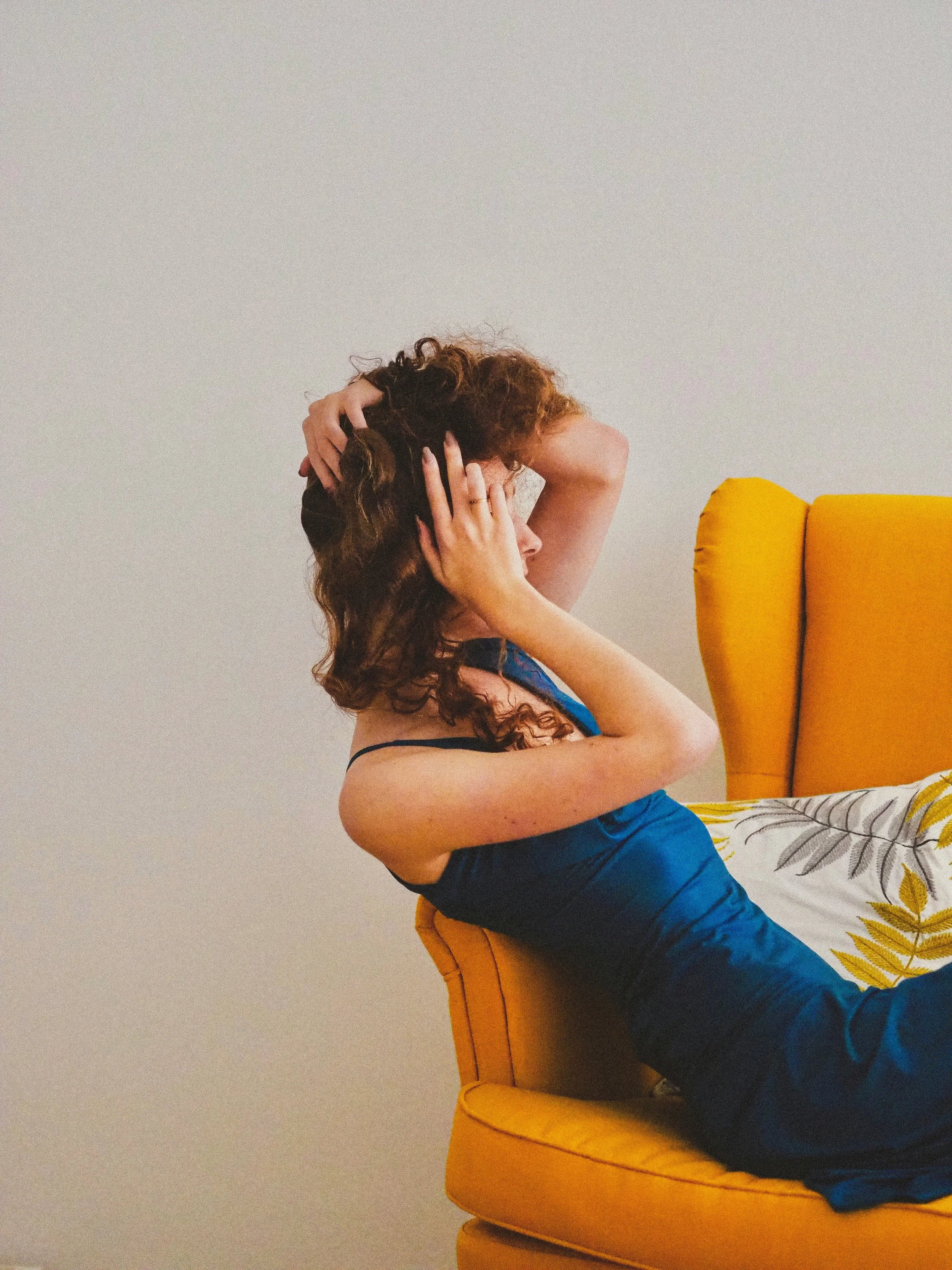 A woman in a yellow chair holds her head