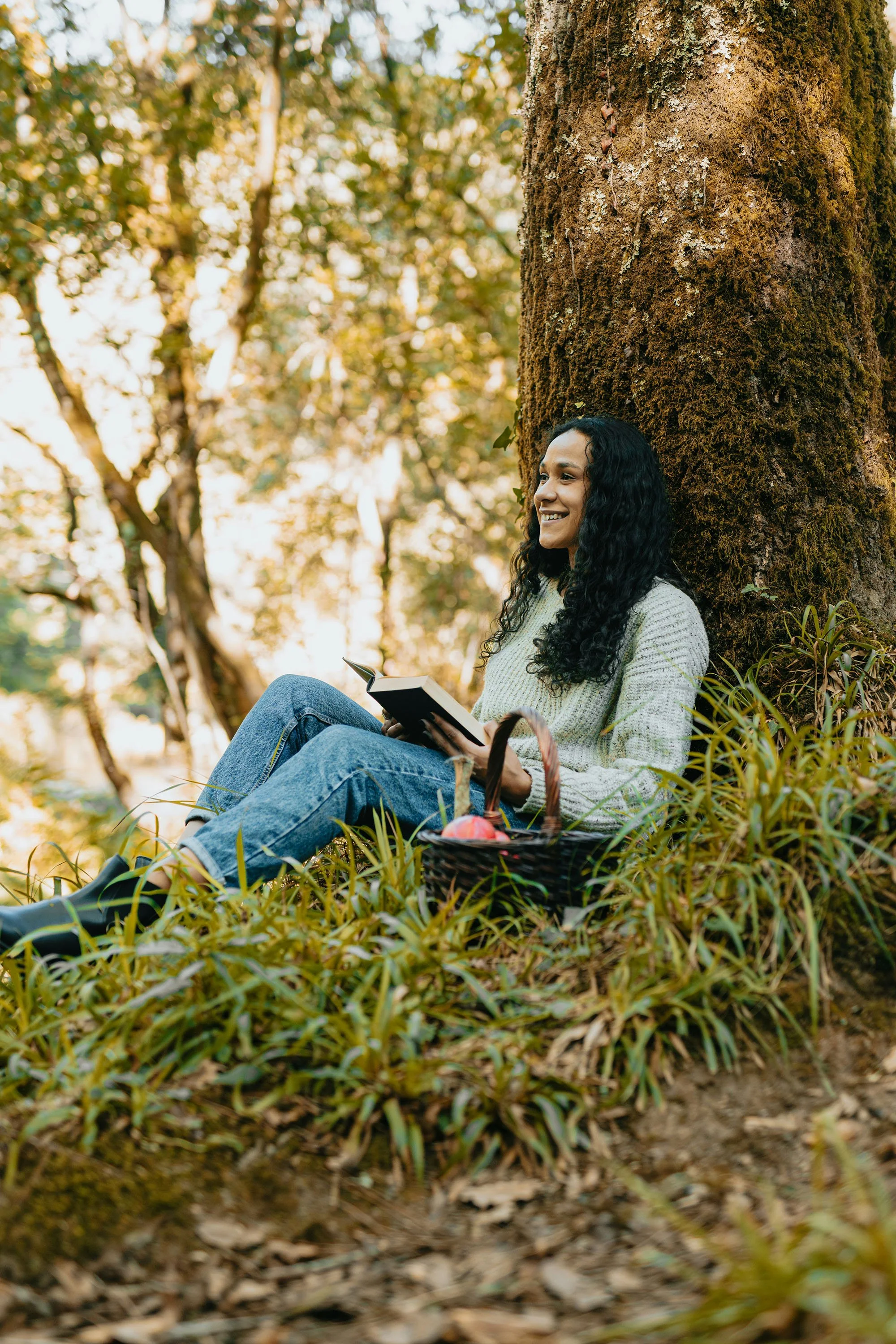 A young woman sits in the grass against a tree