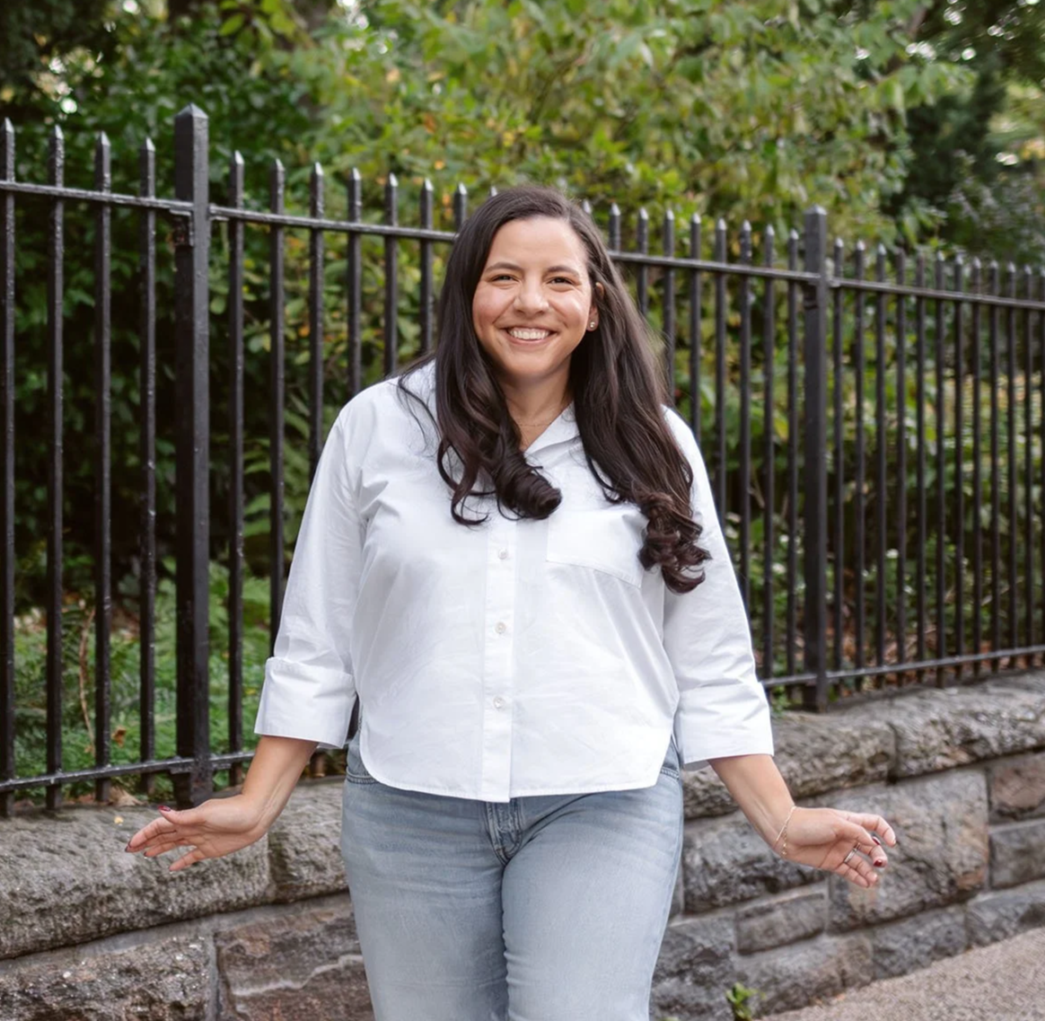 Jessica stands outside and smiles wearing a white button-up