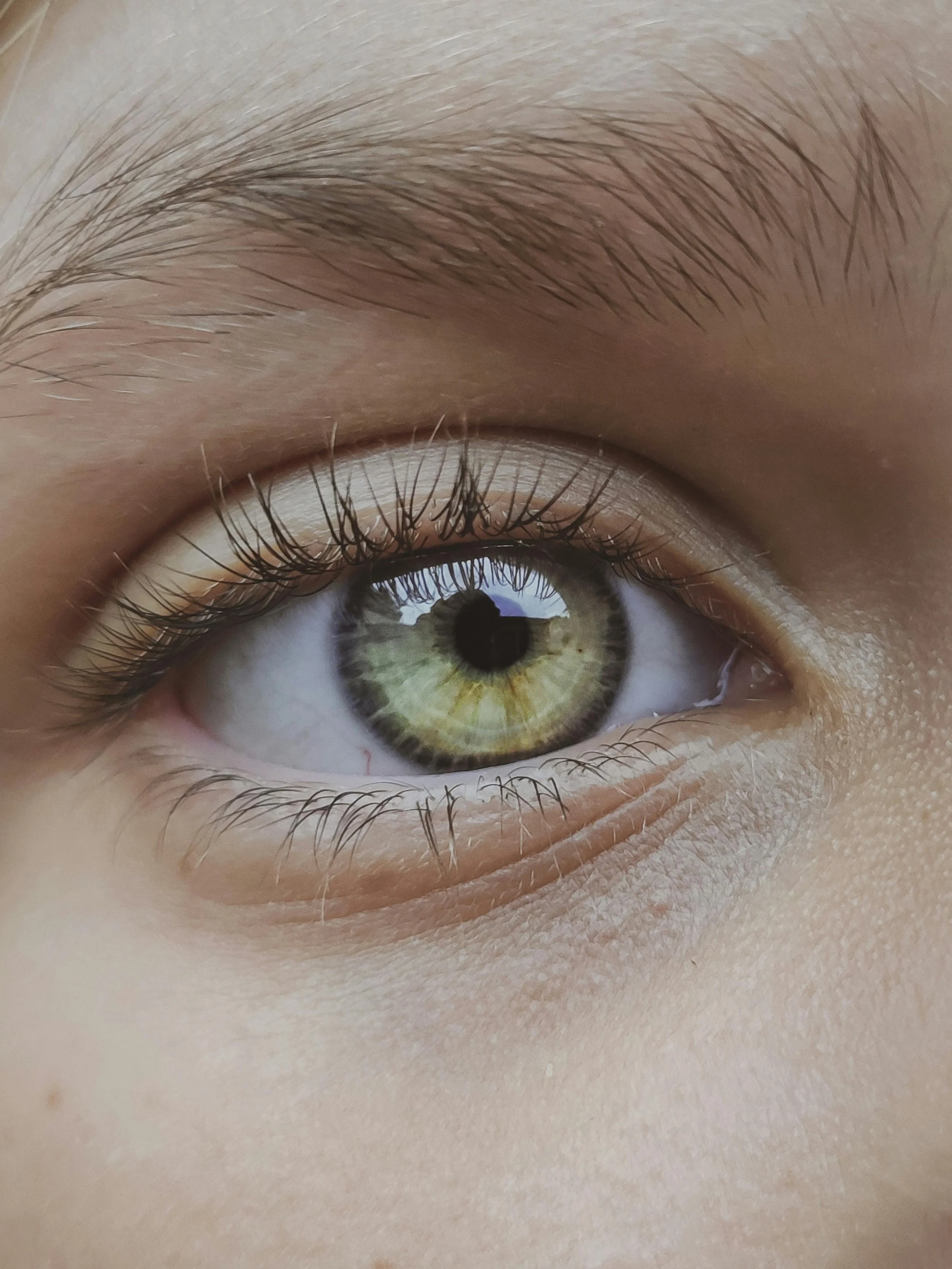Close-up of a human eye with a green iris, detailed eyelashes, and surrounding skin.