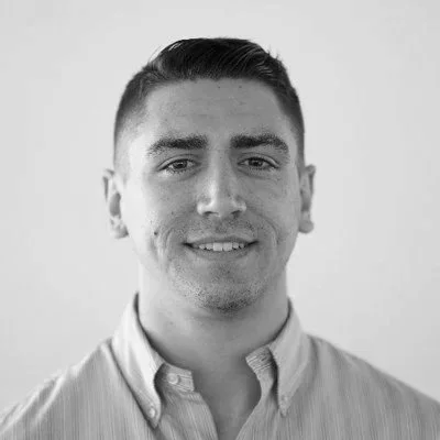 Black and white headshot of a young man with short hair, wearing a collared shirt, smiling at the camera.