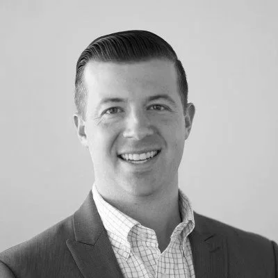 A black and white portrait of a man in a suit smiling at the camera.