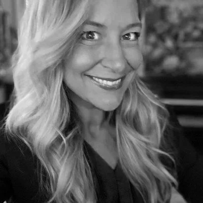 A smiling woman with long, wavy blonde hair in a black top.