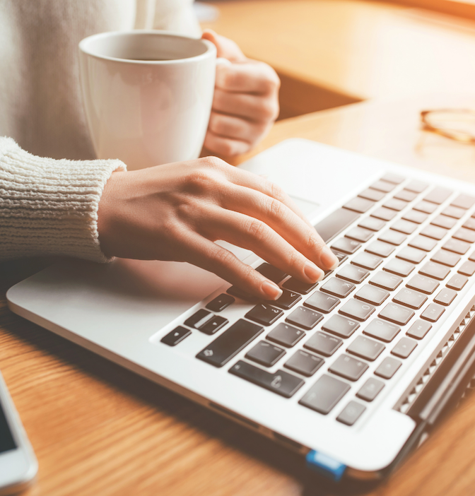woman sitting at computer typing with cup of coffee in hand. professional setting. connecting and networking.