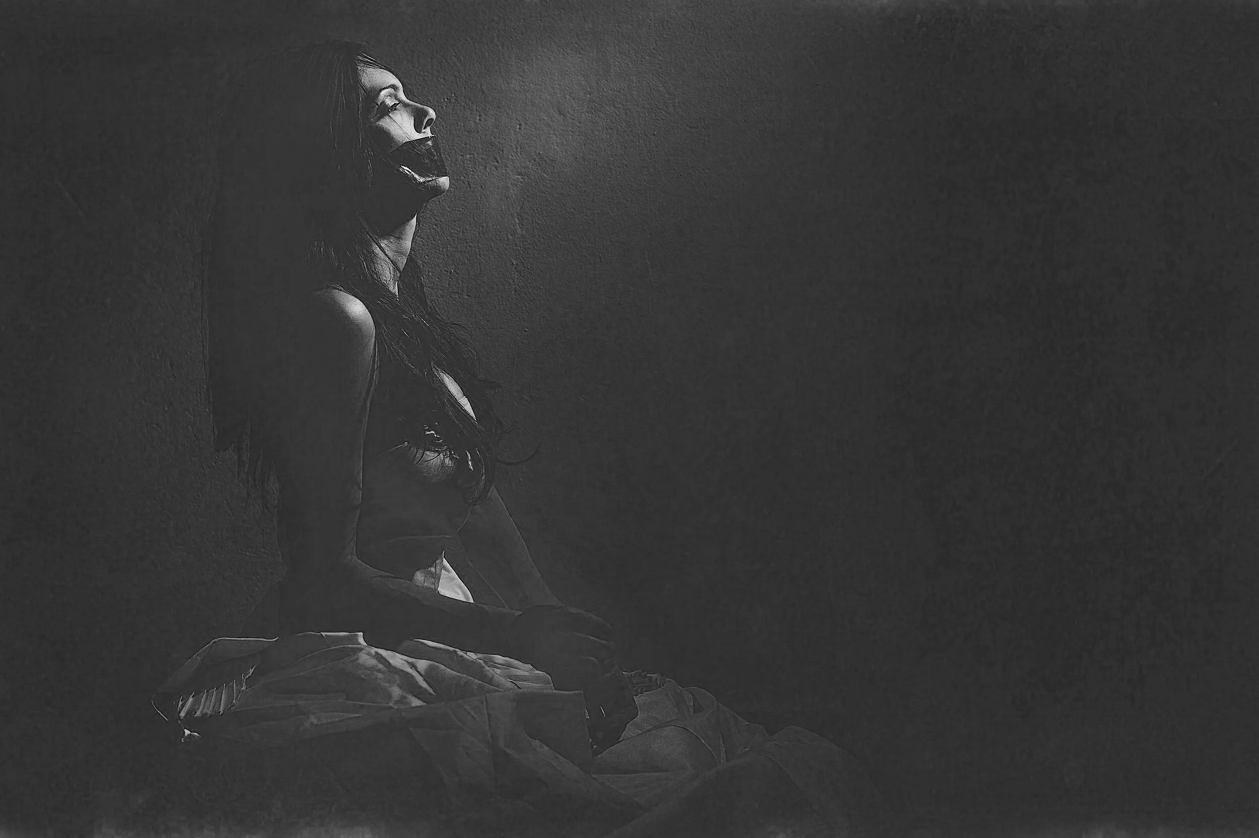 A woman sitting against a textured wall with her head tilted back and mouth open, depicted in black and white with a high contrast and dramatic lighting.